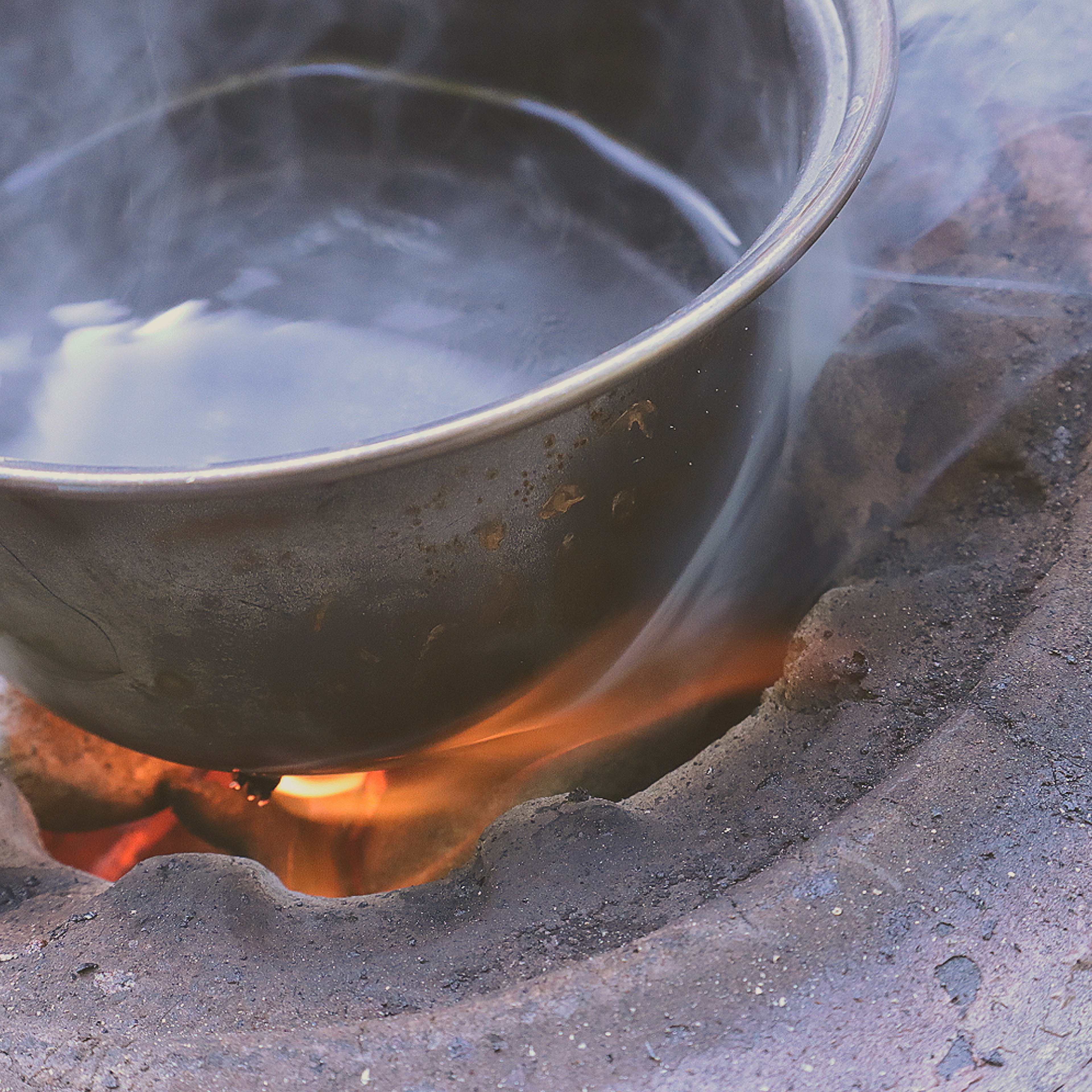 A pot heating water over an open flame with smoke rising