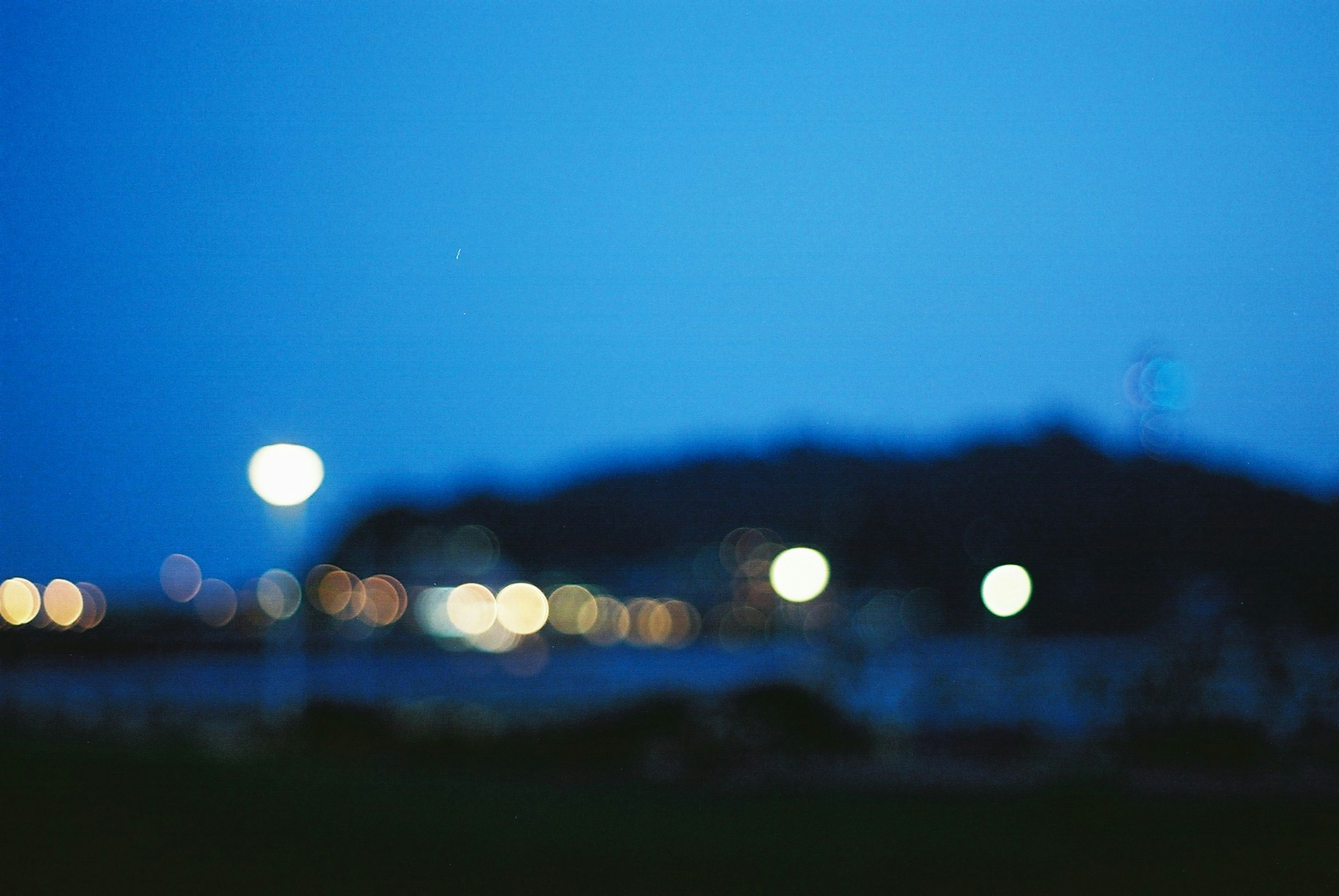 Blurred blue night sky with glowing streetlights and silhouette of distant hills