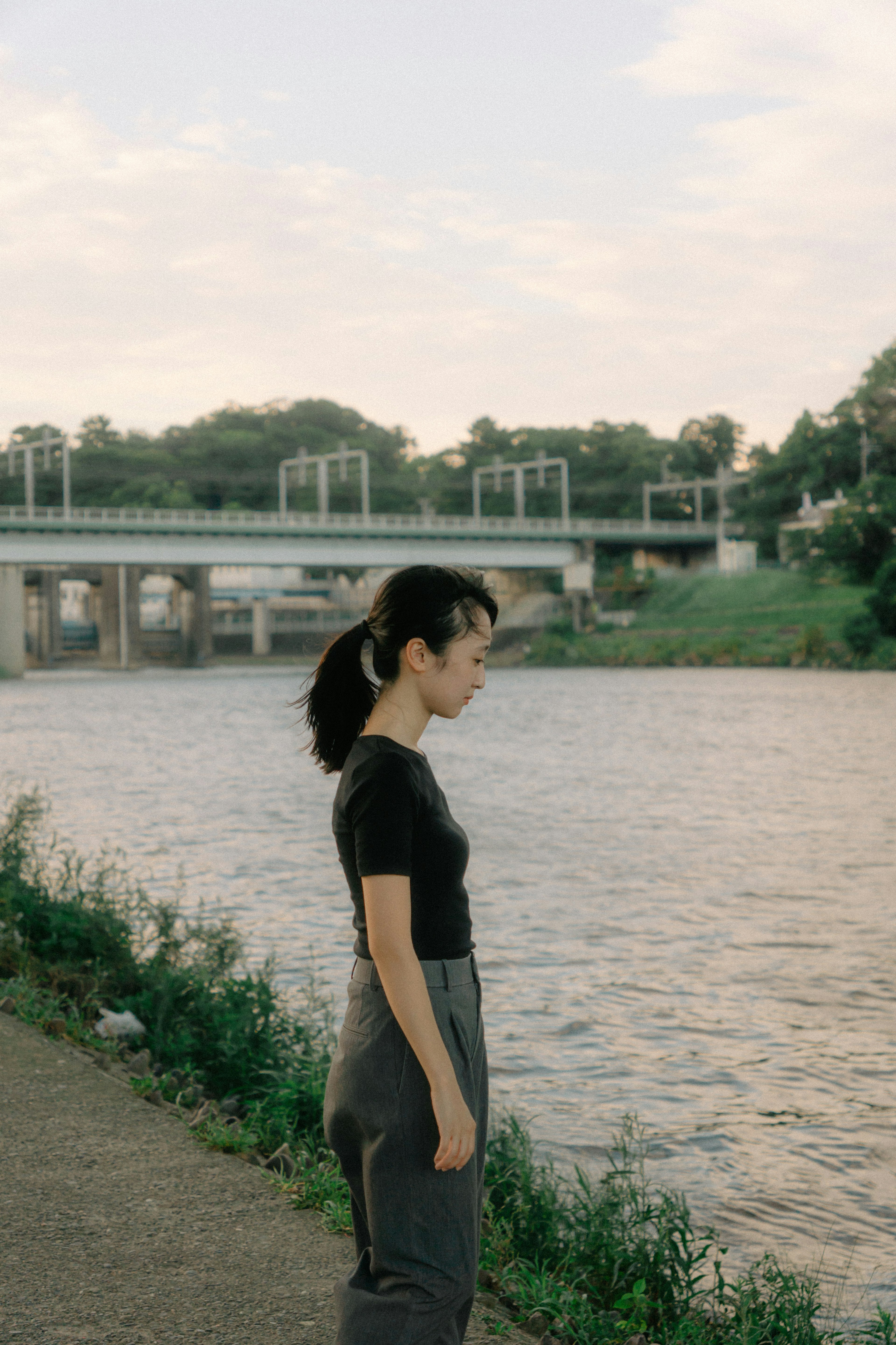 Side profile of a woman contemplating by the river with a bridge in the background