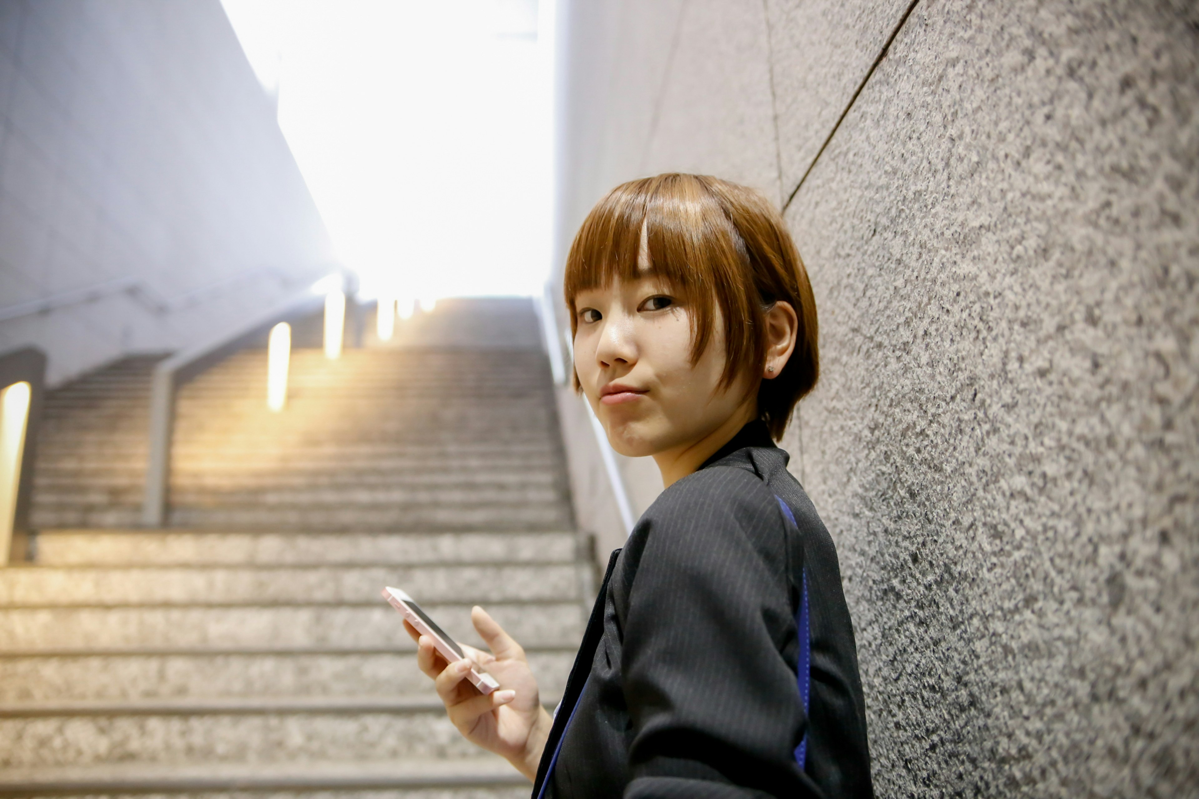 Short-haired woman holding a smartphone near stairs