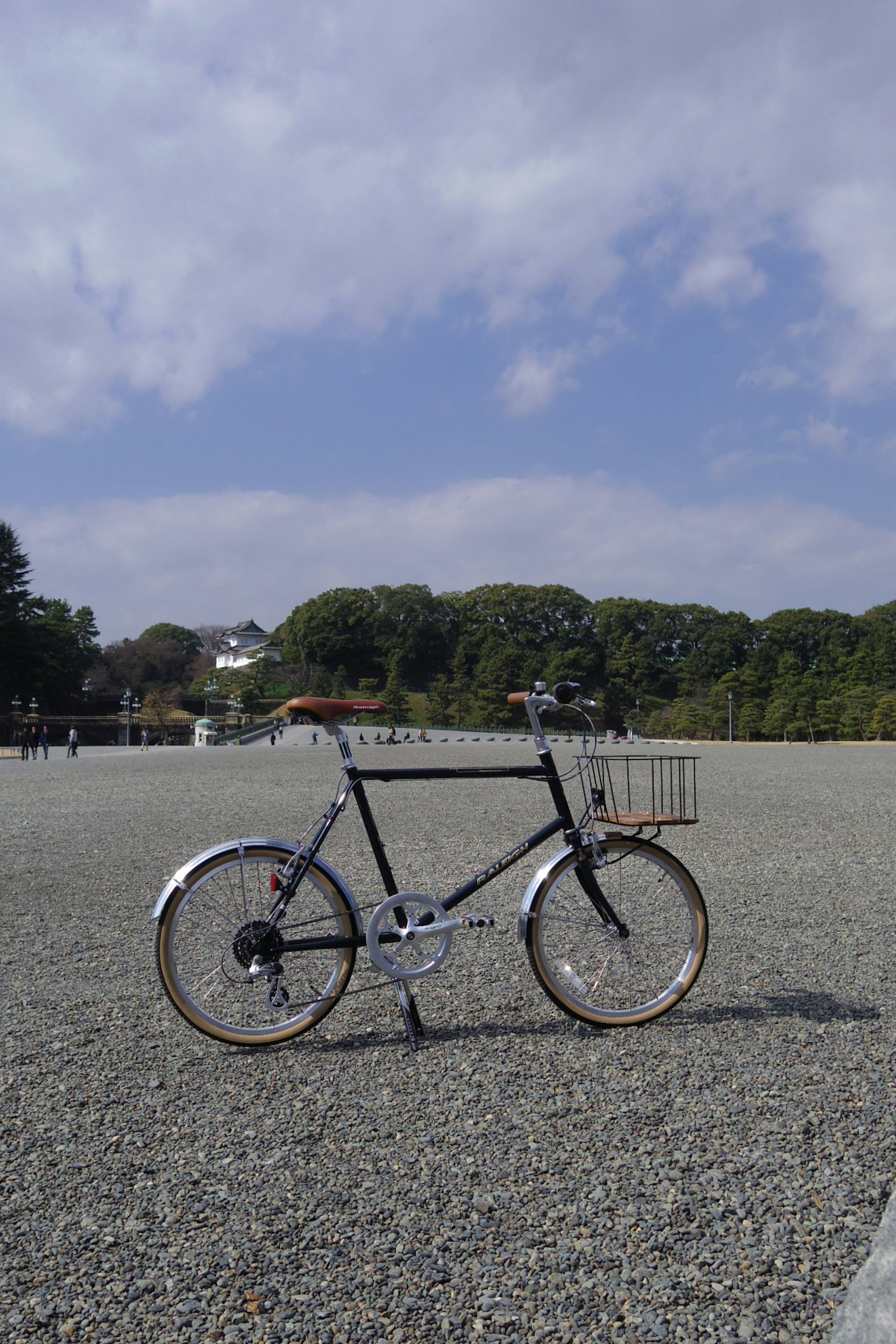 A black bicycle standing on a wide gravel field under a blue sky