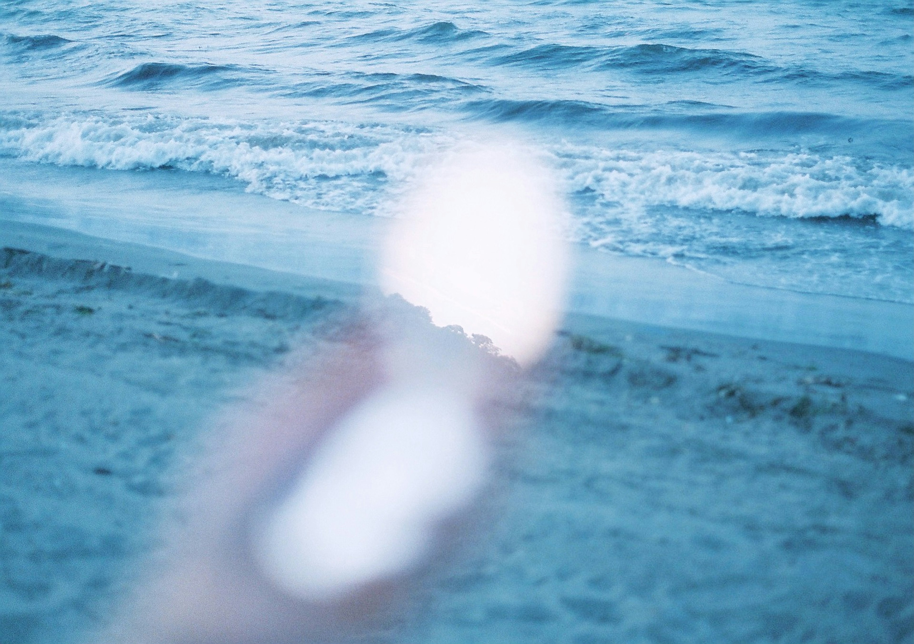 Mano che tiene un oggetto luminoso vicino alla spiaggia con onde oceaniche