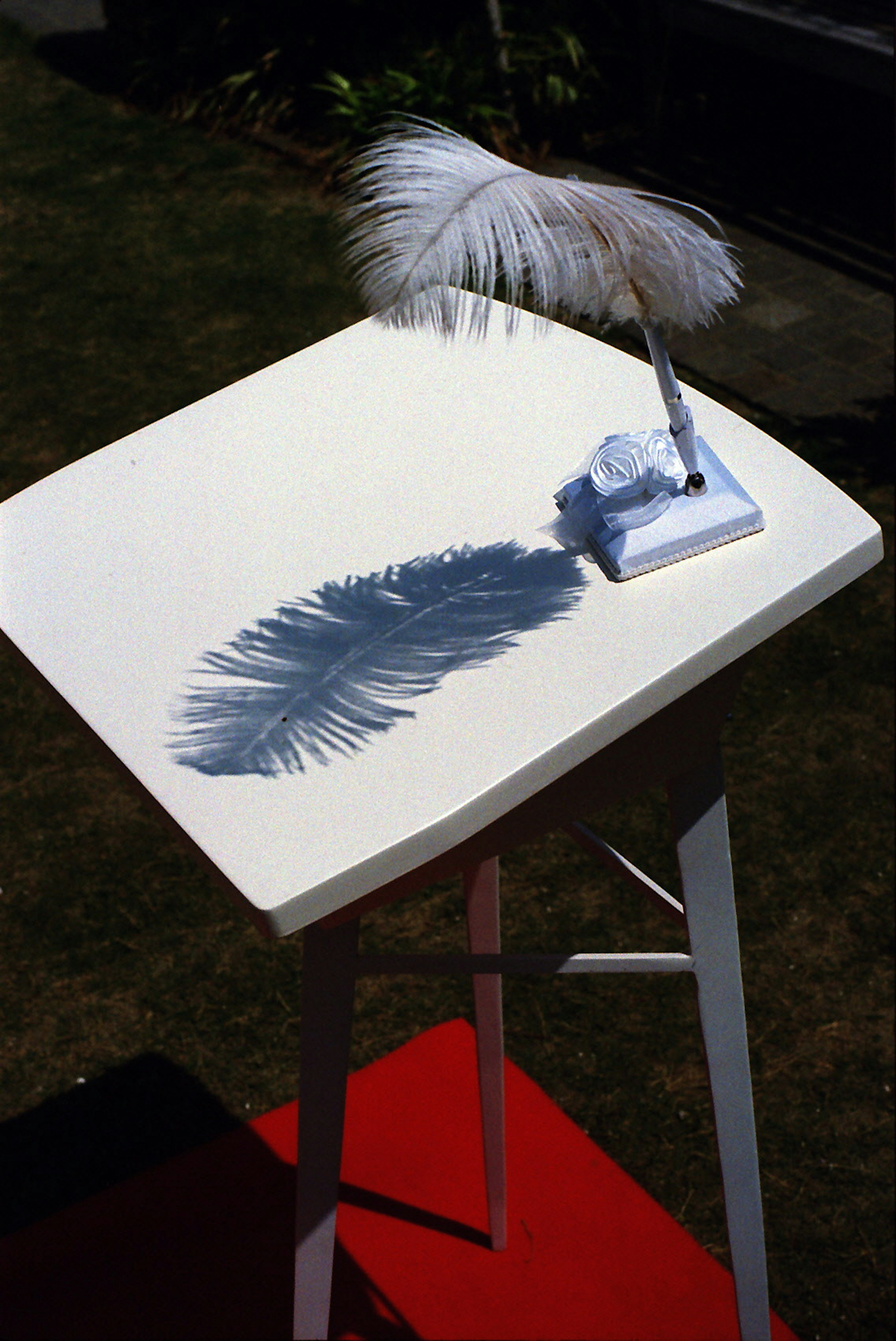 A white table with a feather quill and its shadow