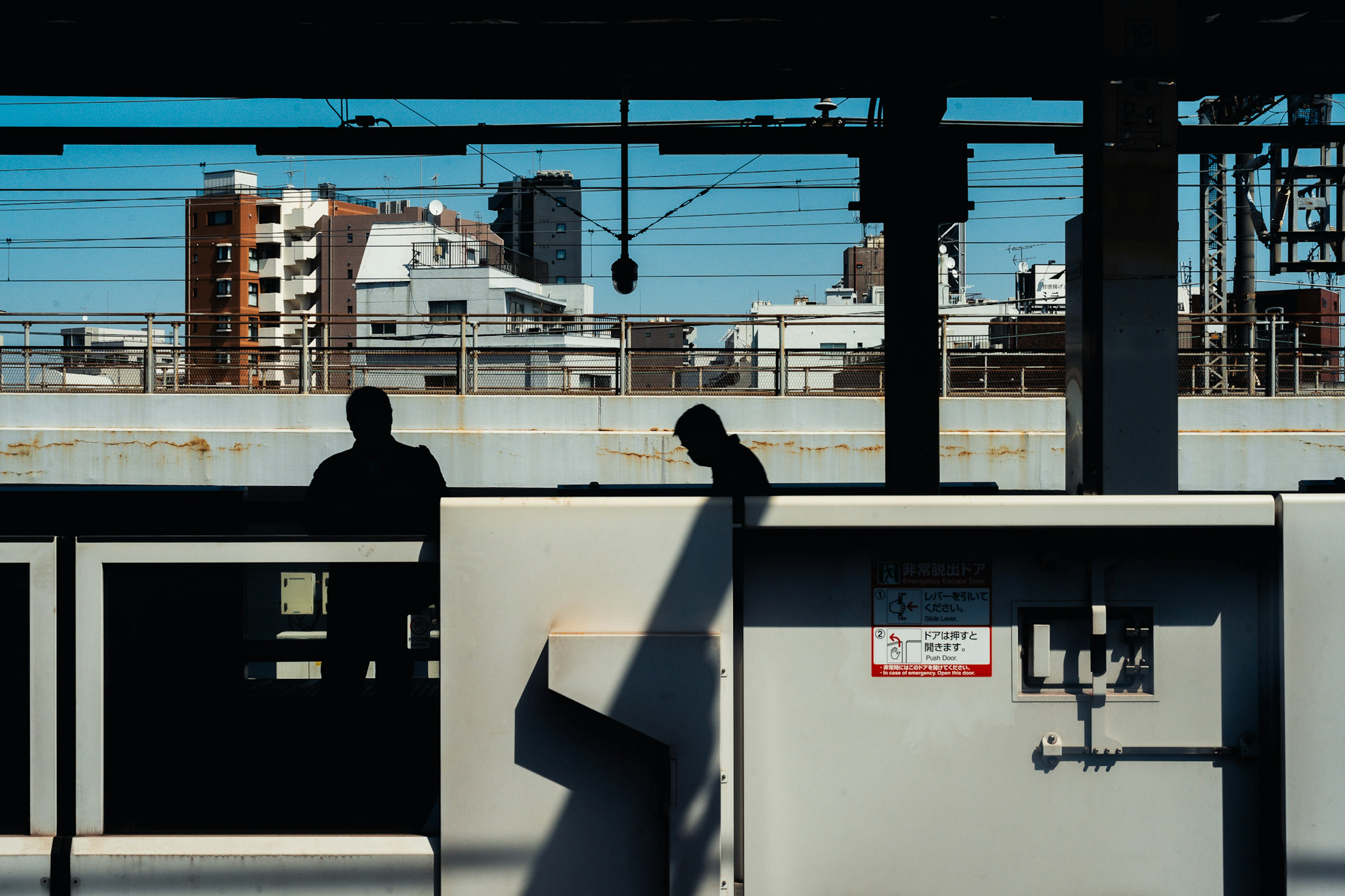 Silhouetted figures on a train platform with a city skyline in the background