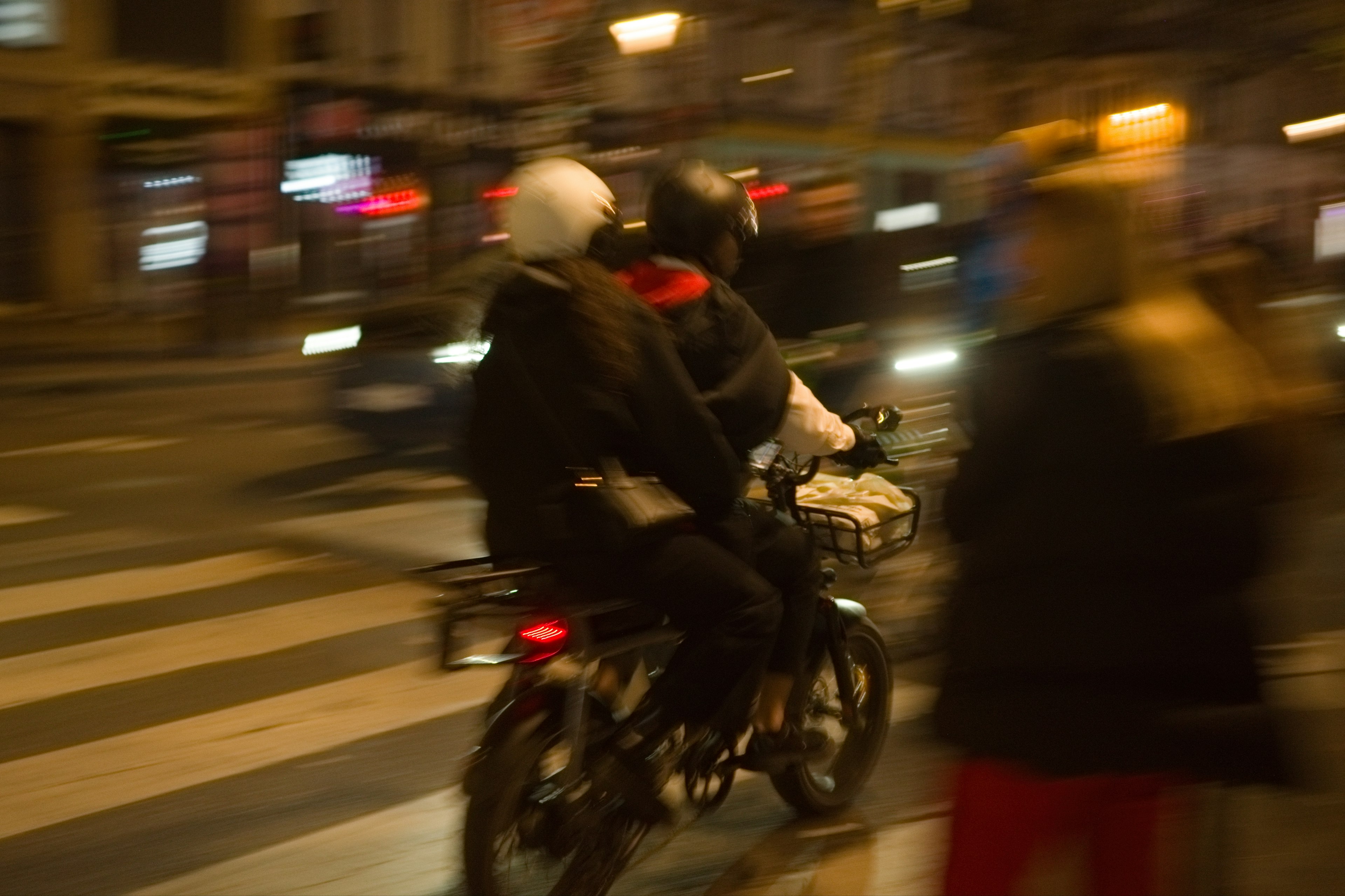 Deux motocyclistes sur une moto dans une rue animée la nuit avec un flou de mouvement