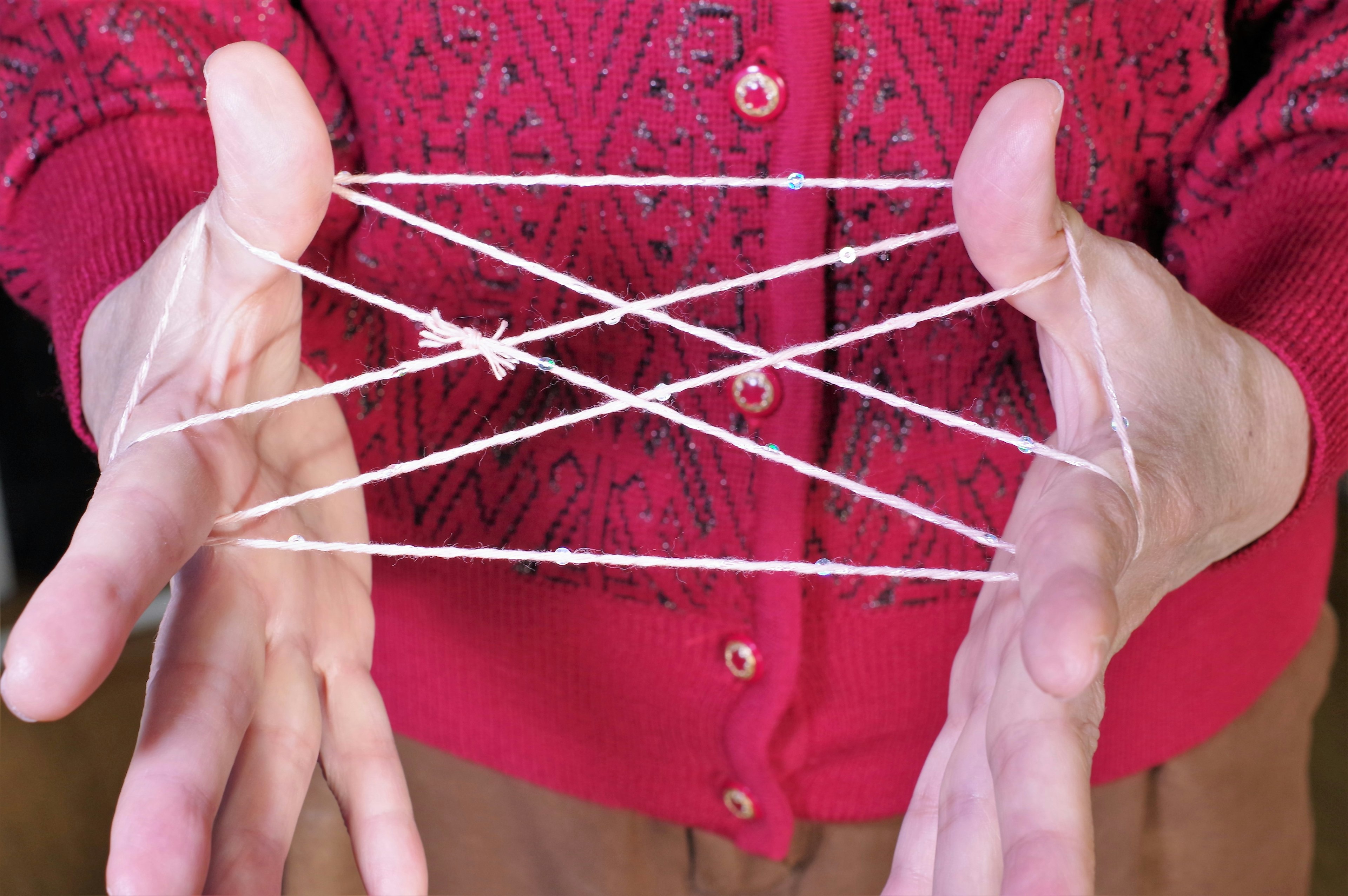 Pattern of string stretched between hands wearing a red sweater