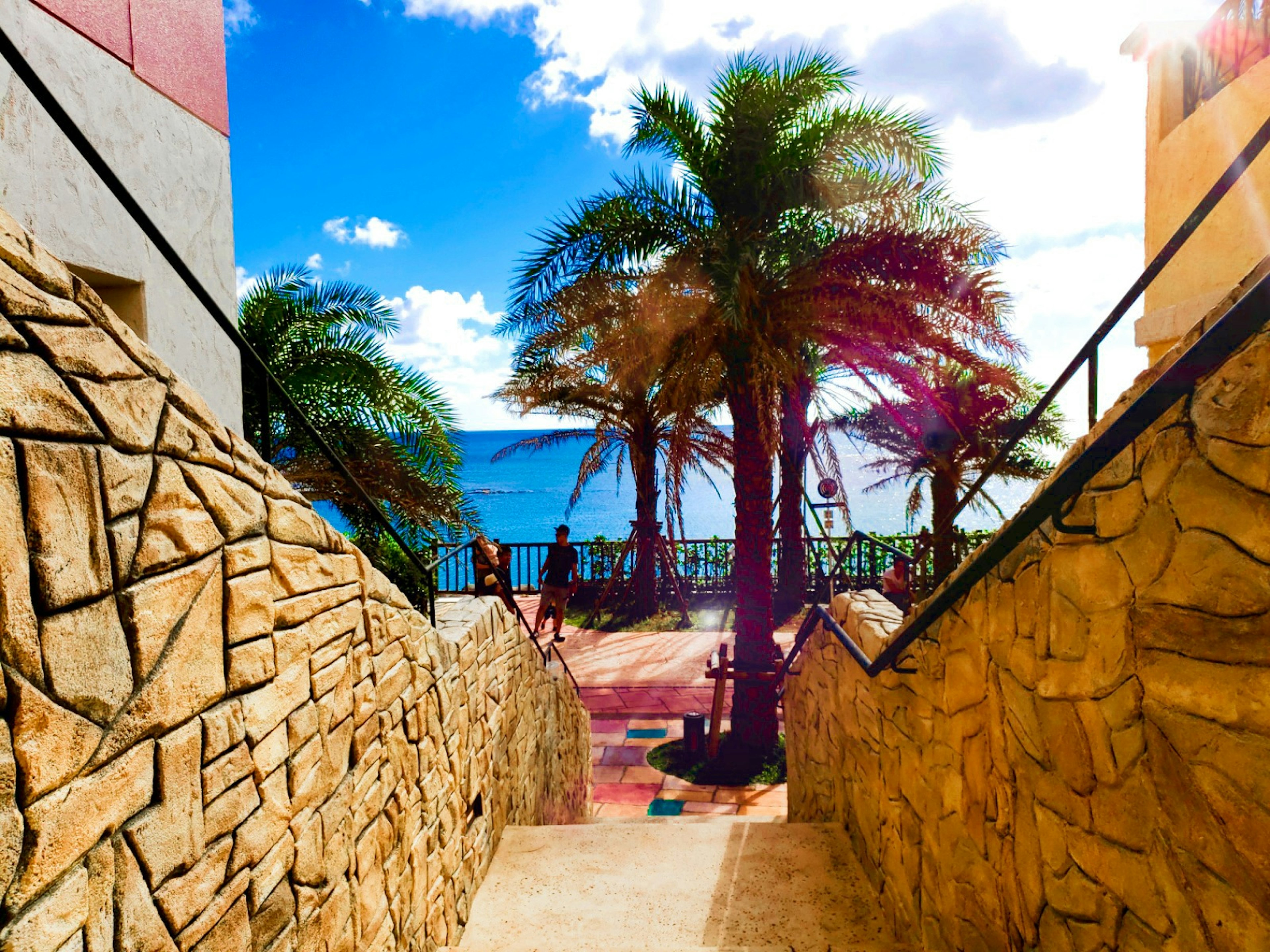 Escalera que lleva a una playa con palmeras y océano azul brillante