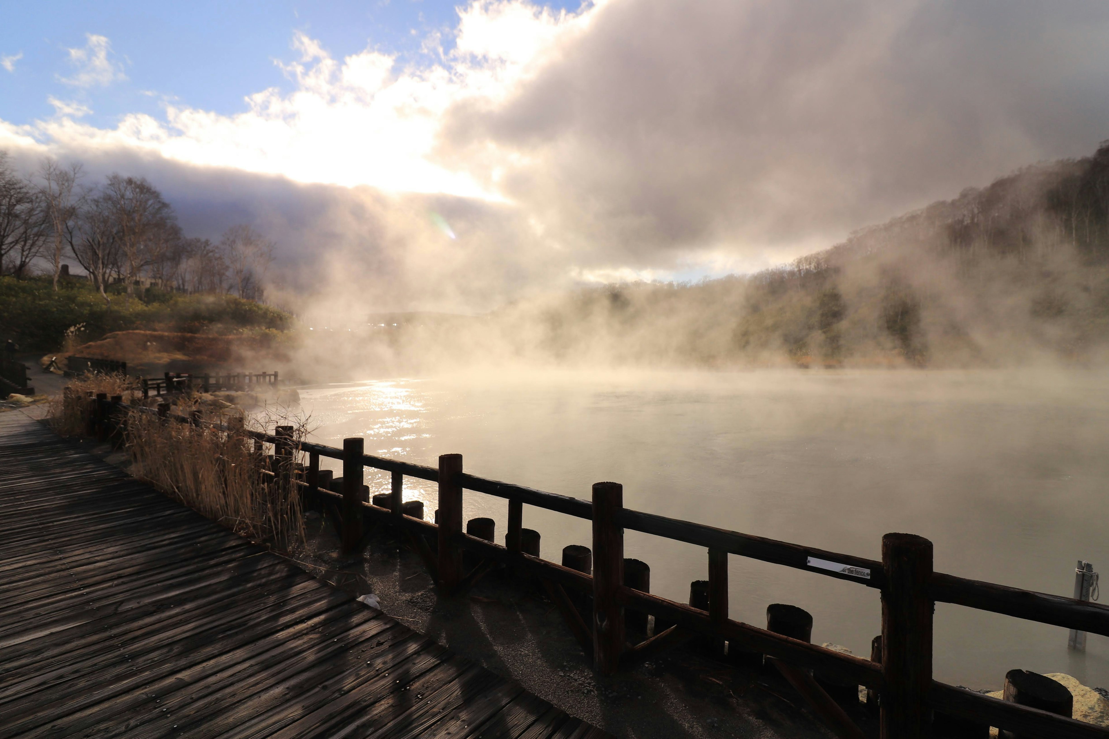 Lago brumoso con pasarela de madera y montañas escénicas