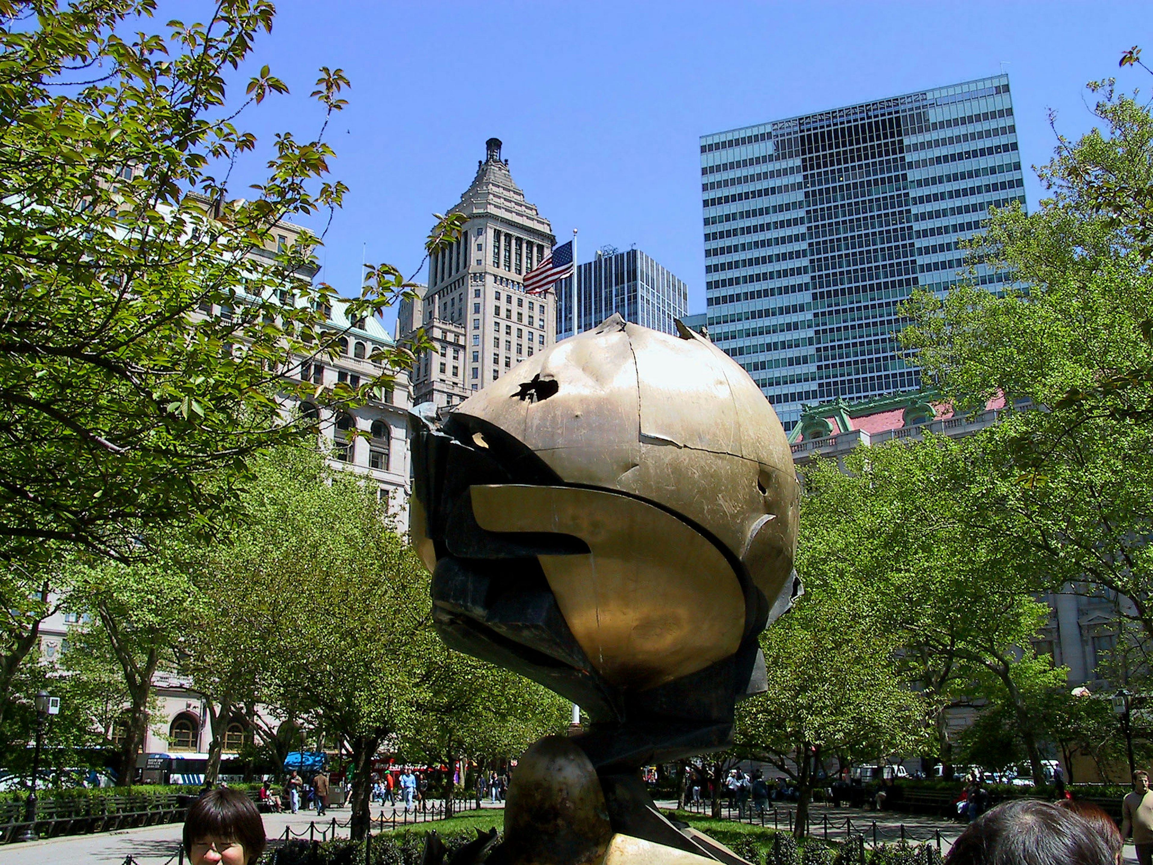 Golden globe sculpture in a park with skyscrapers in the background