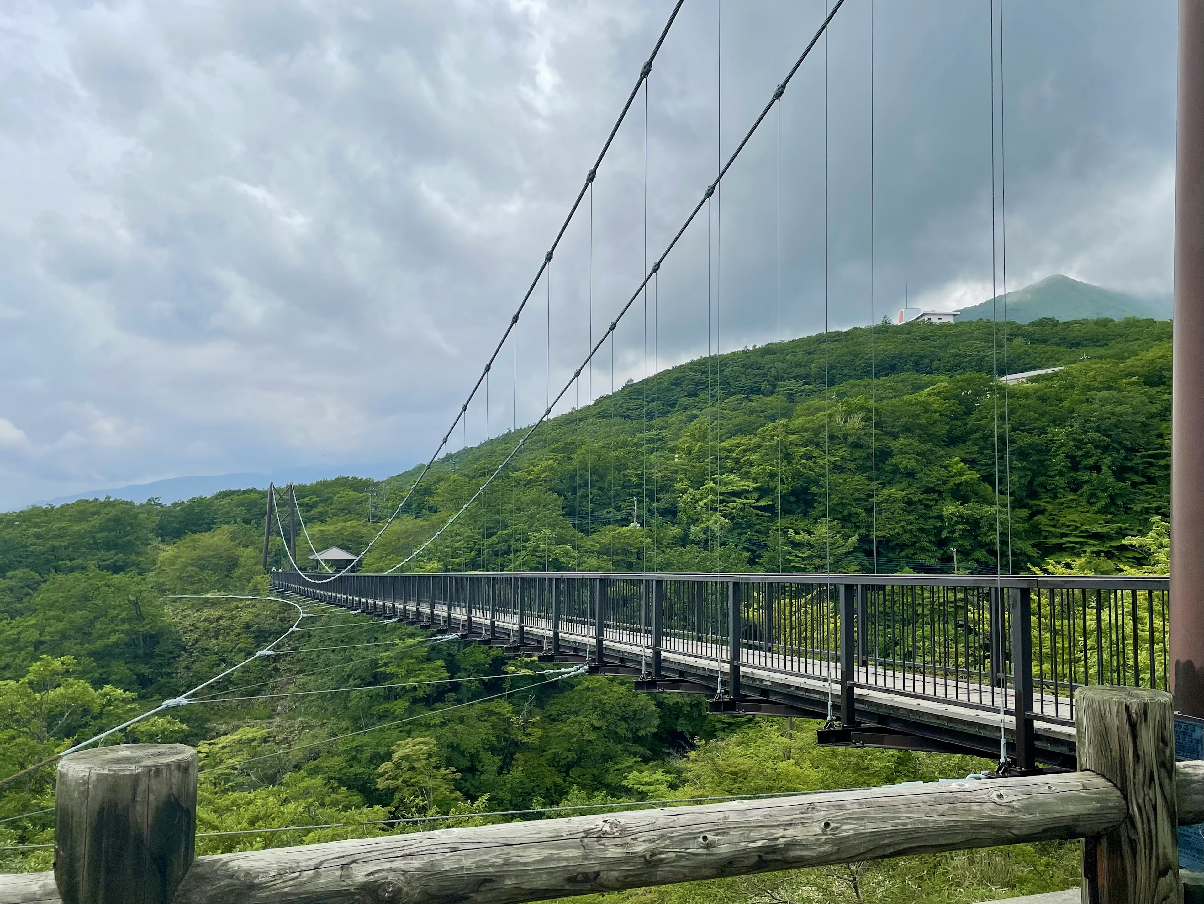 Suspension bridge over lush green mountains under a cloudy sky