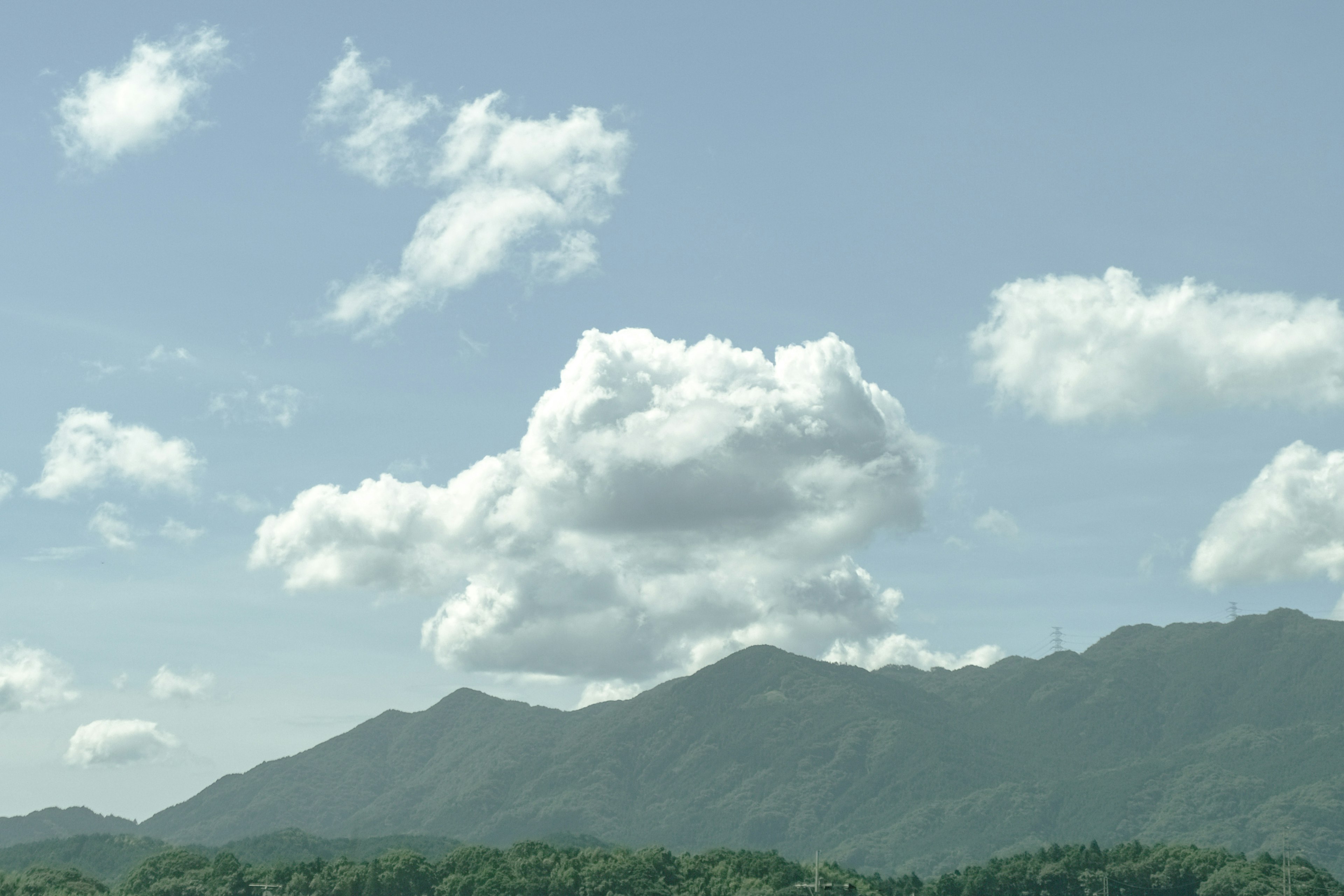 青空と白い雲に囲まれた緑の山々の風景