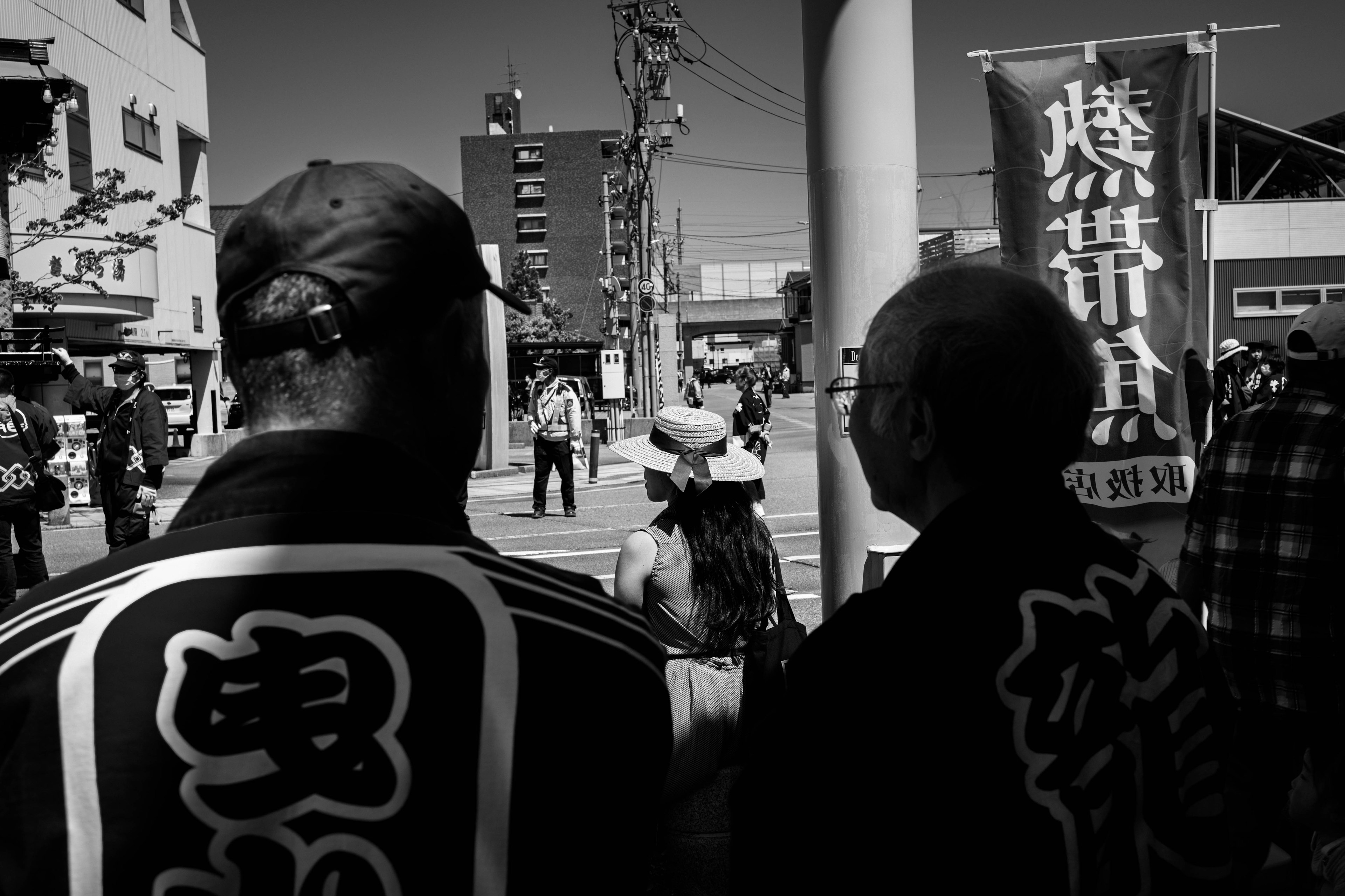 Escena de festival en blanco y negro con dos hombres en ropa tradicional vistos desde atrás