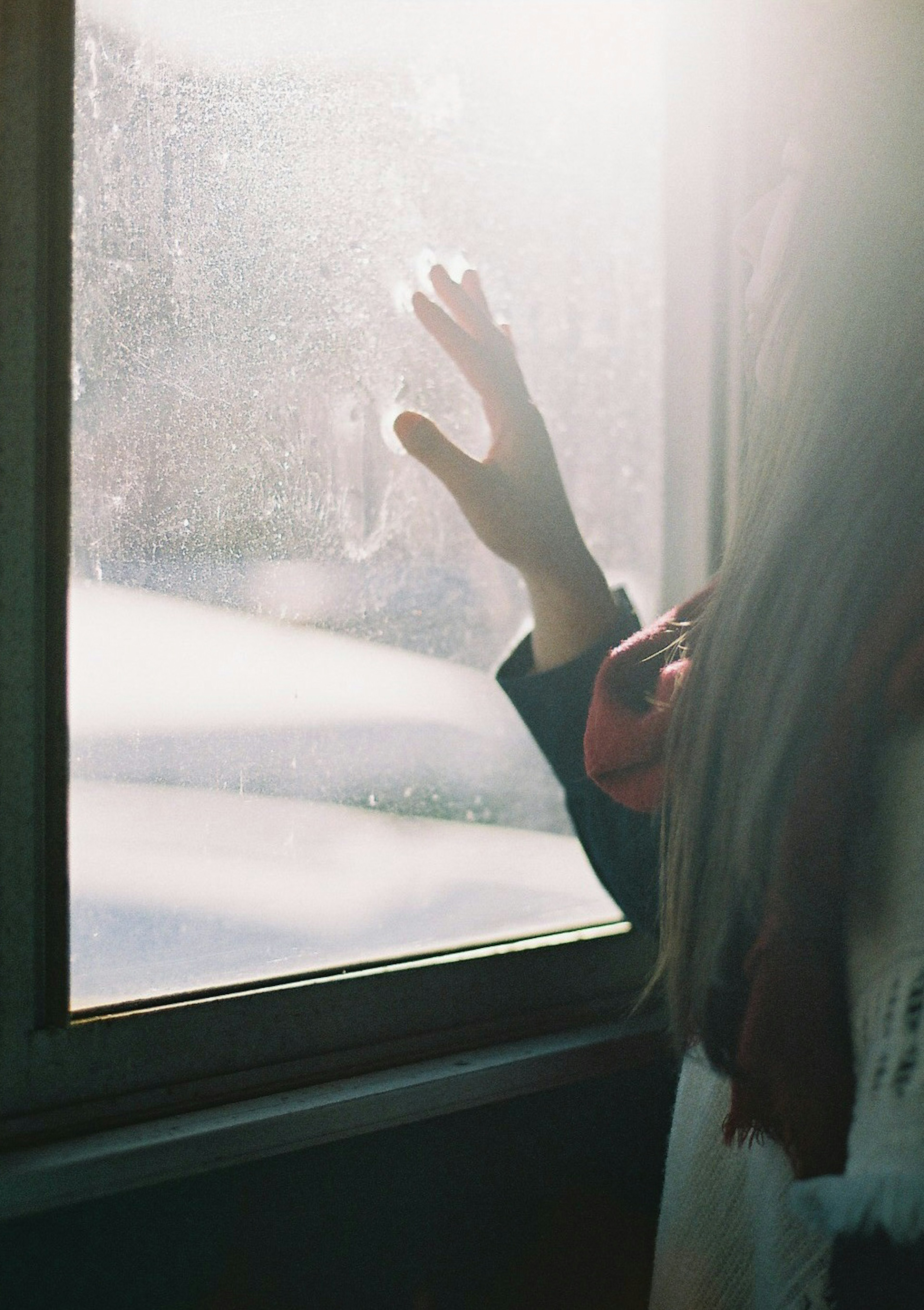 Eine Hand einer Frau, die zu einem Fenster greift, während Sonnenlicht die Szene beleuchtet