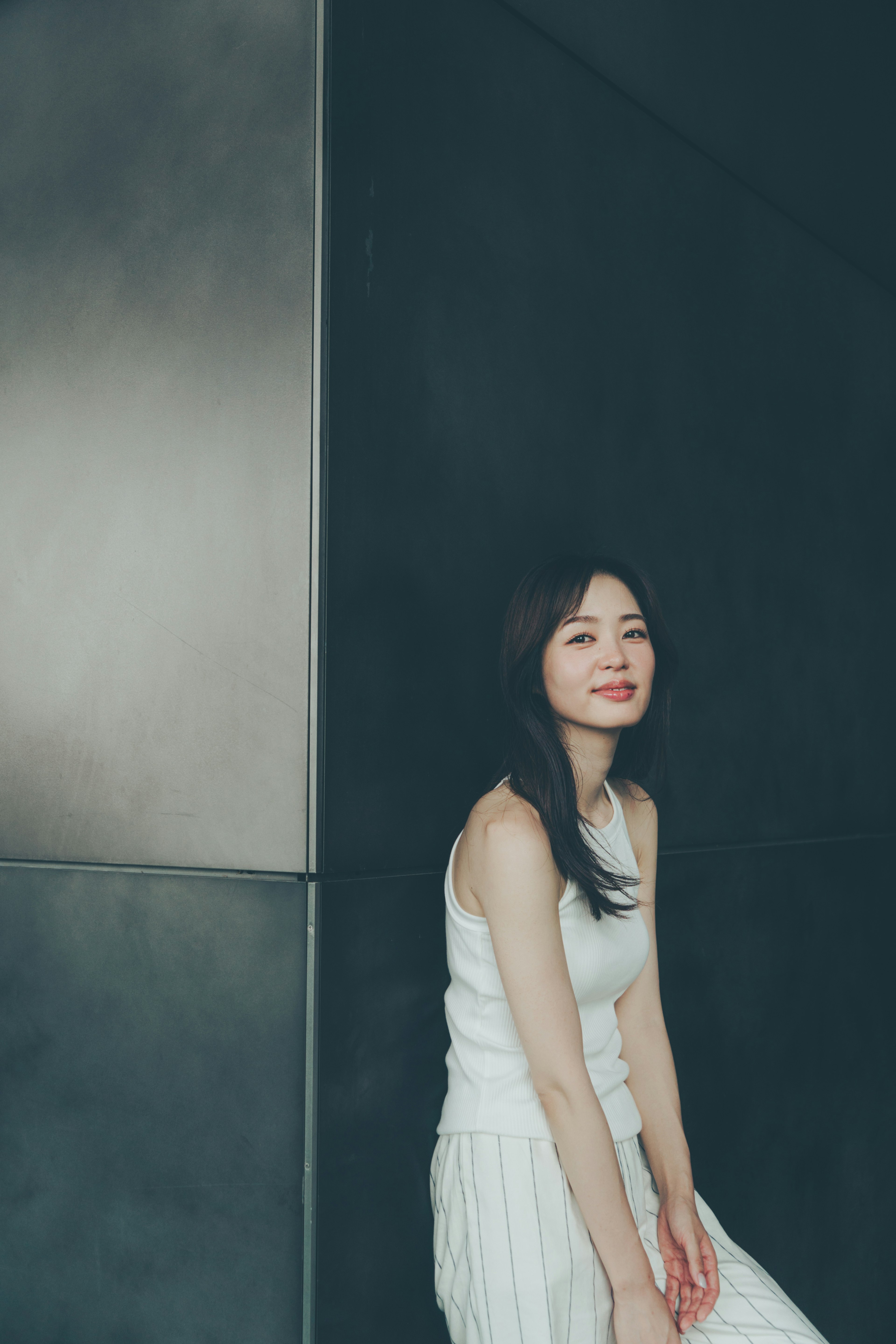 Una mujer con un vestido blanco sonriendo mientras está sentada contra un fondo moderno y simple