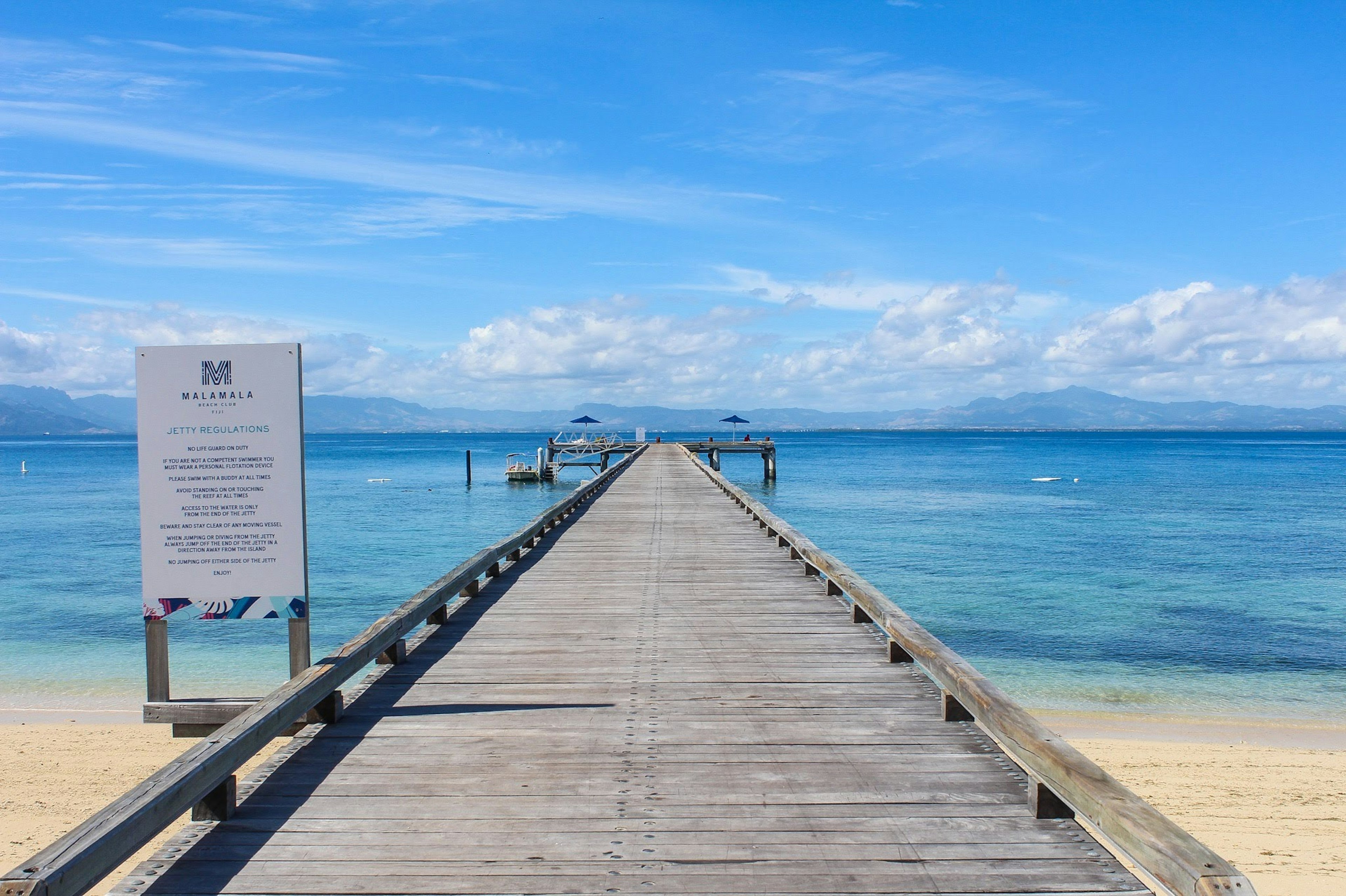 Holzpier, der sich über klares blaues Wasser unter einem hellen Himmel erstreckt