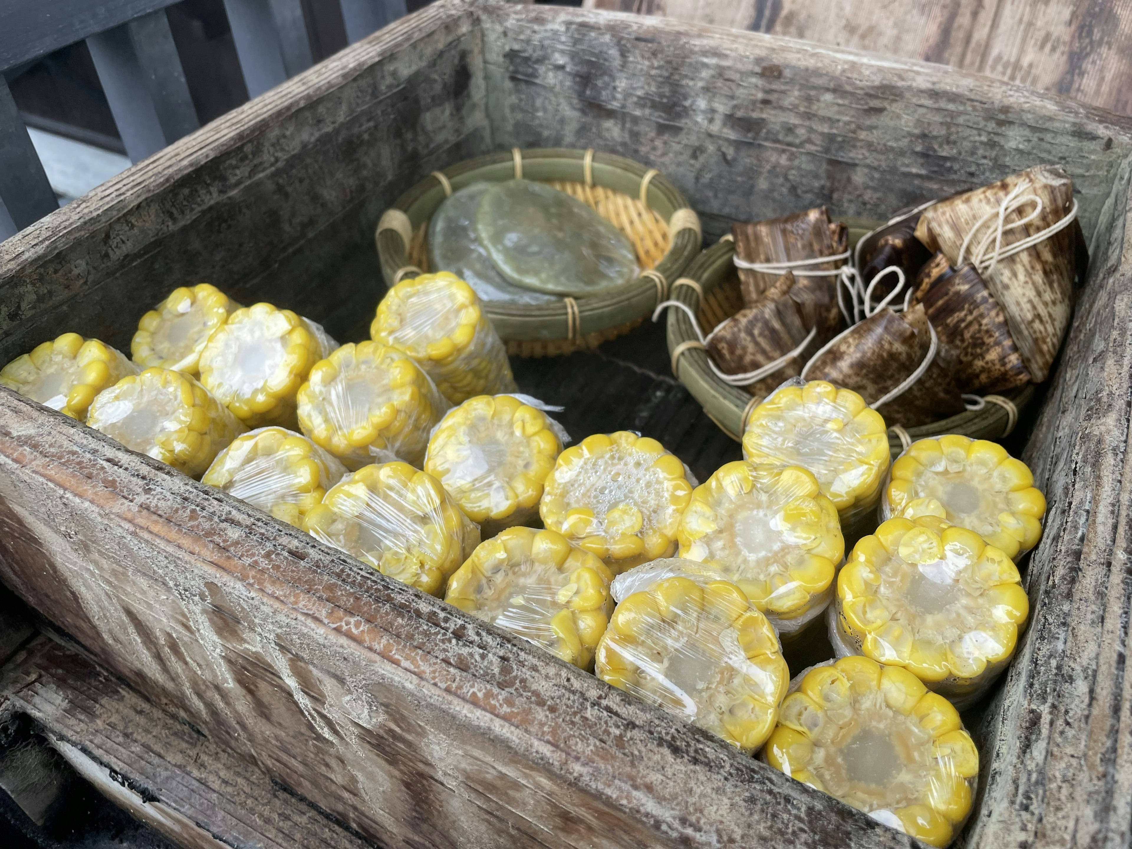 Boîte en bois contenant des aliments enveloppés de jaune et des contenants en bambou