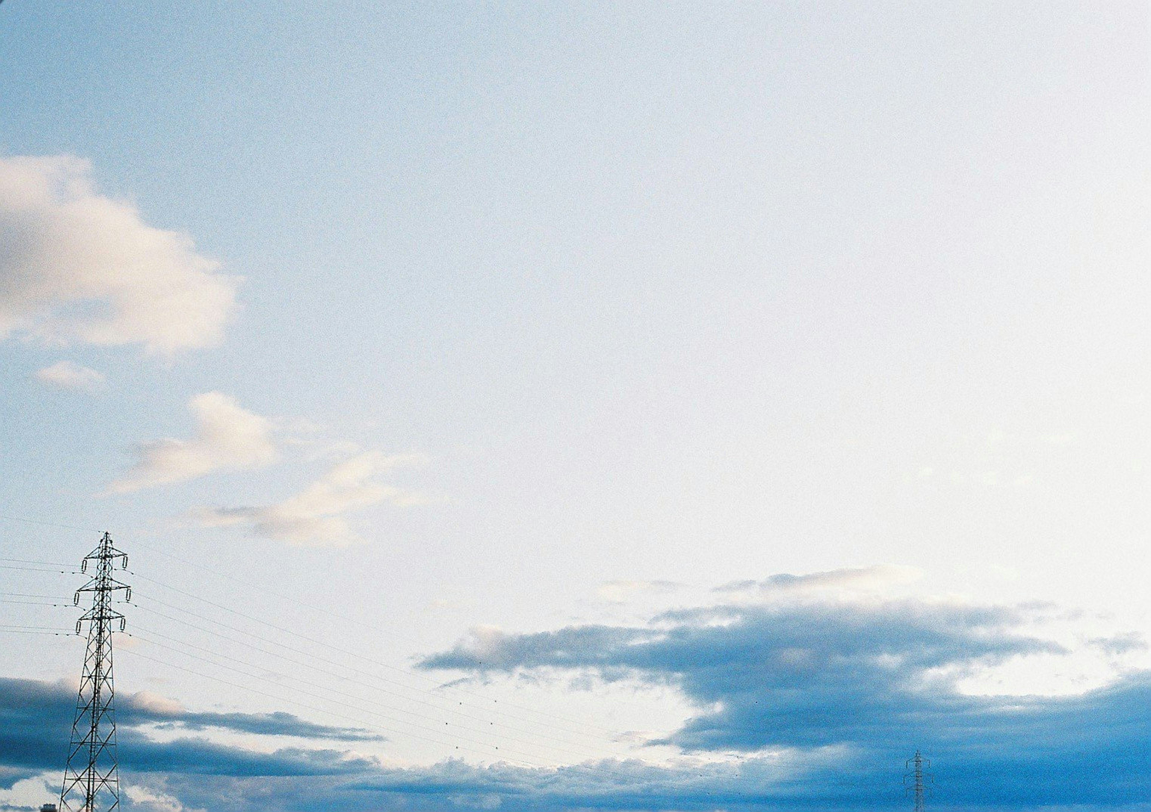 Landschaft mit einem hohen Strommast vor blauem Himmel