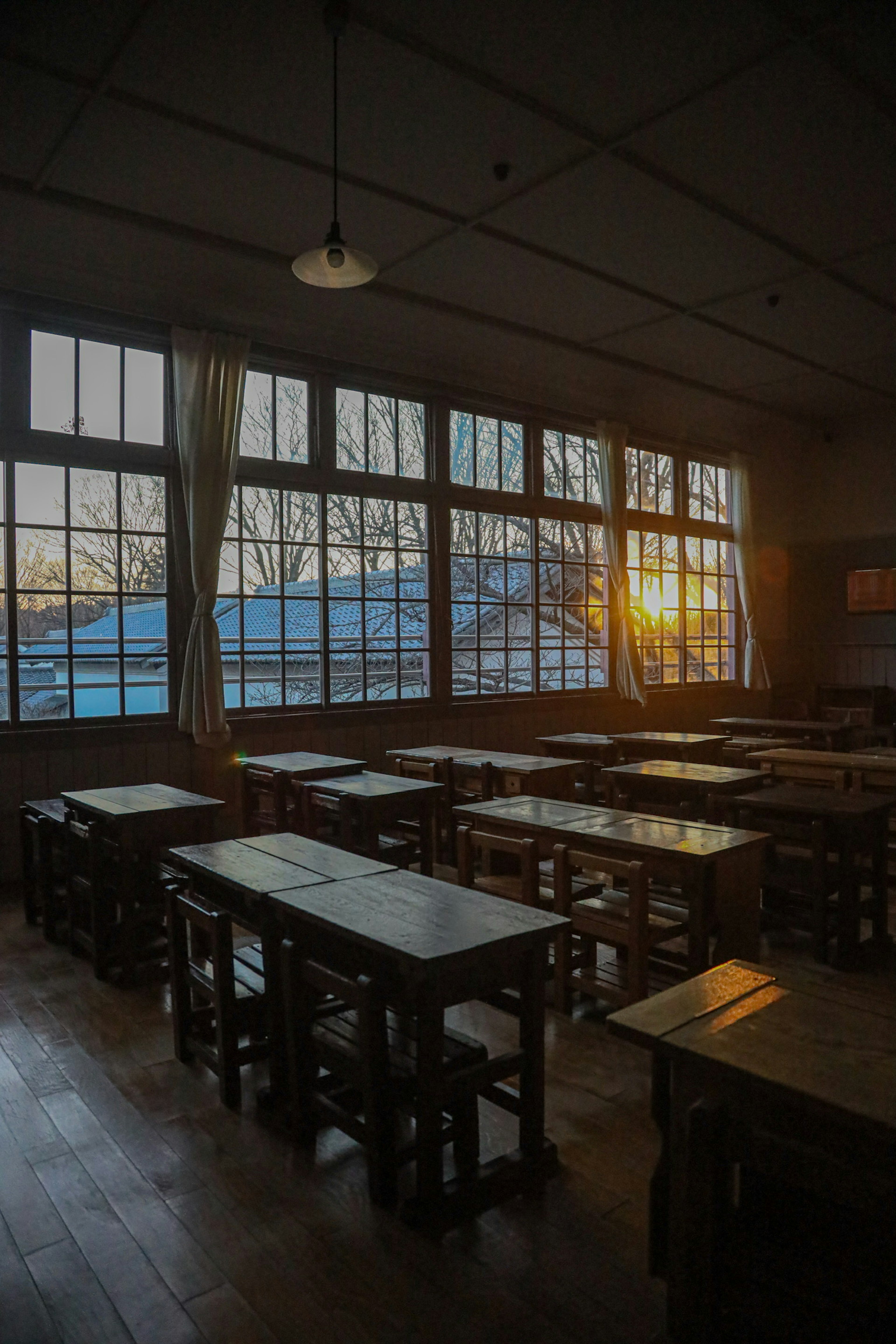 Klassenzimmer mit Holztischen und -stühlen, die vom Sonnenuntergang durch große Fenster beleuchtet werden