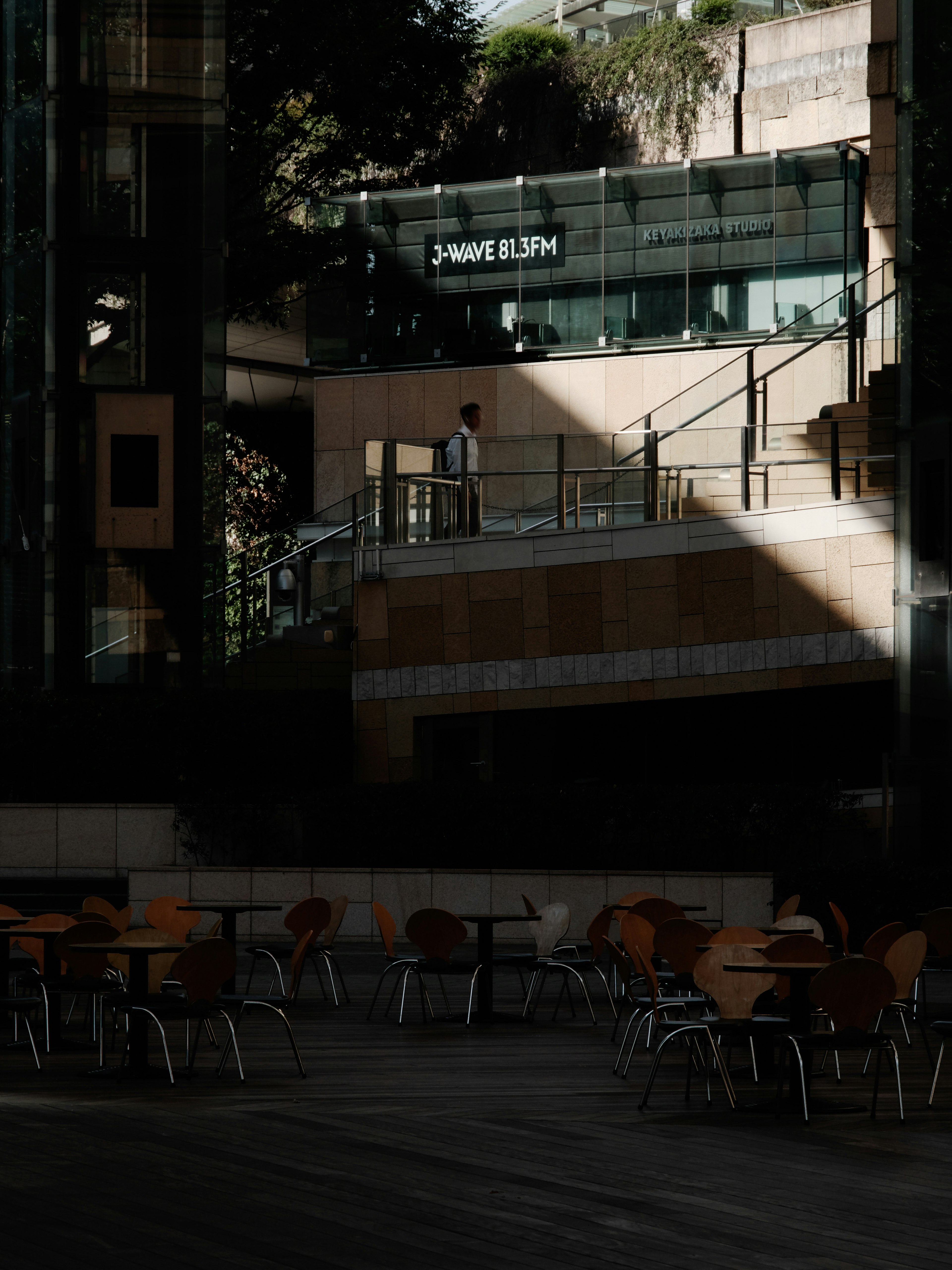 Vista exterior de un edificio con mesas y sillas de café en una zona oscura