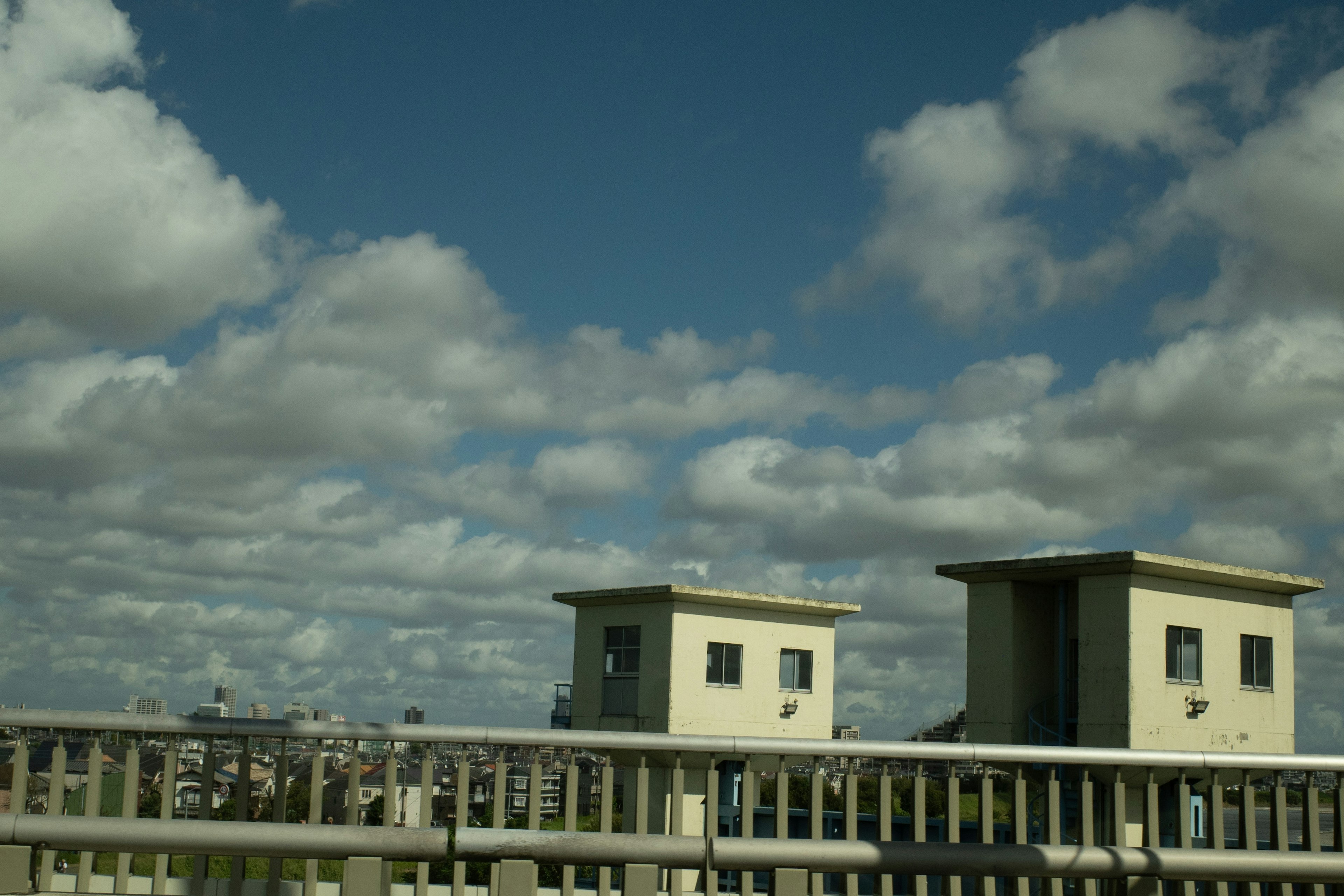 青空と白い雲の下にある二つの建物と橋の風景