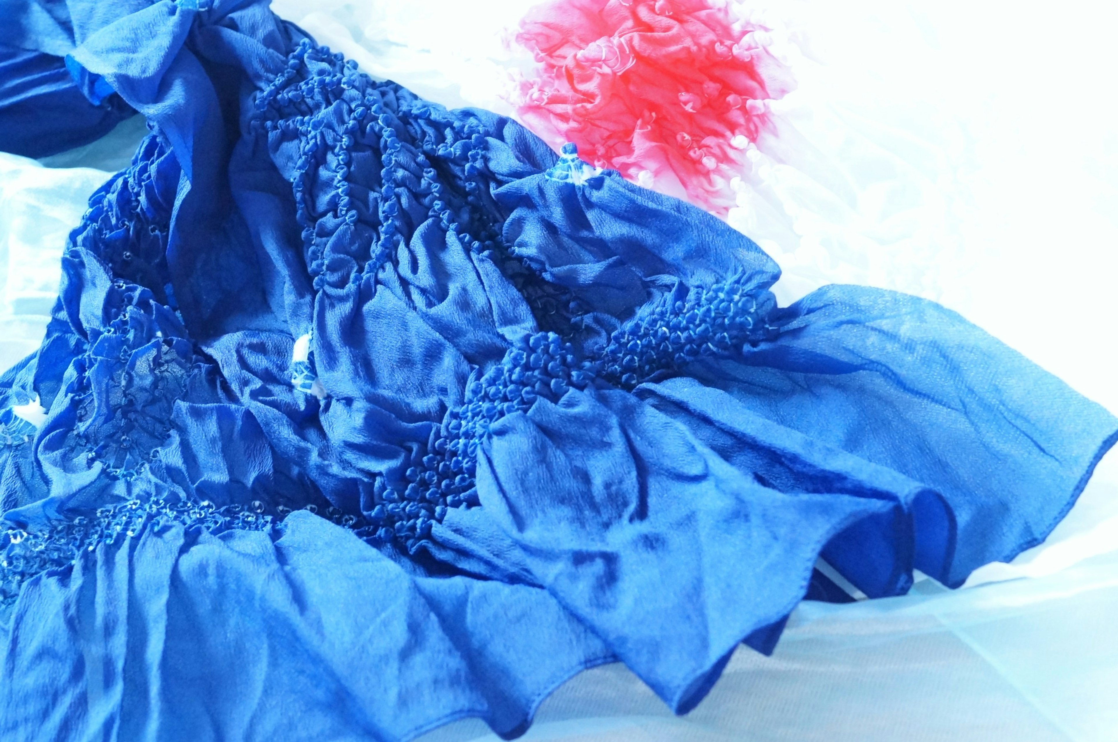 Imagen que presenta una tela de vestido azul con texturas únicas y un elemento decorativo rojo