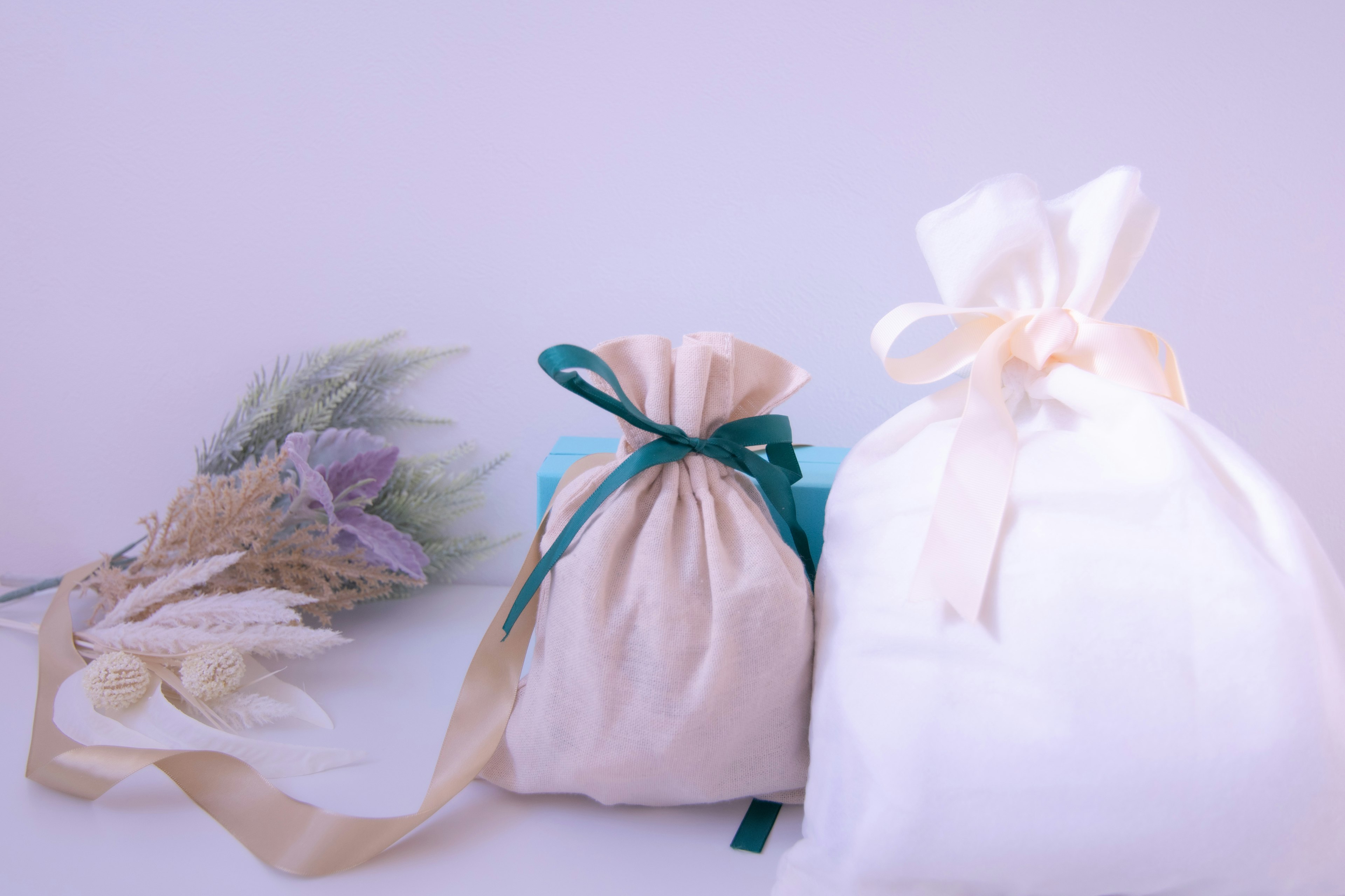 Deux sacs-cadeaux en tissu de couleurs douces à côté d'un bouquet de fleurs séchées