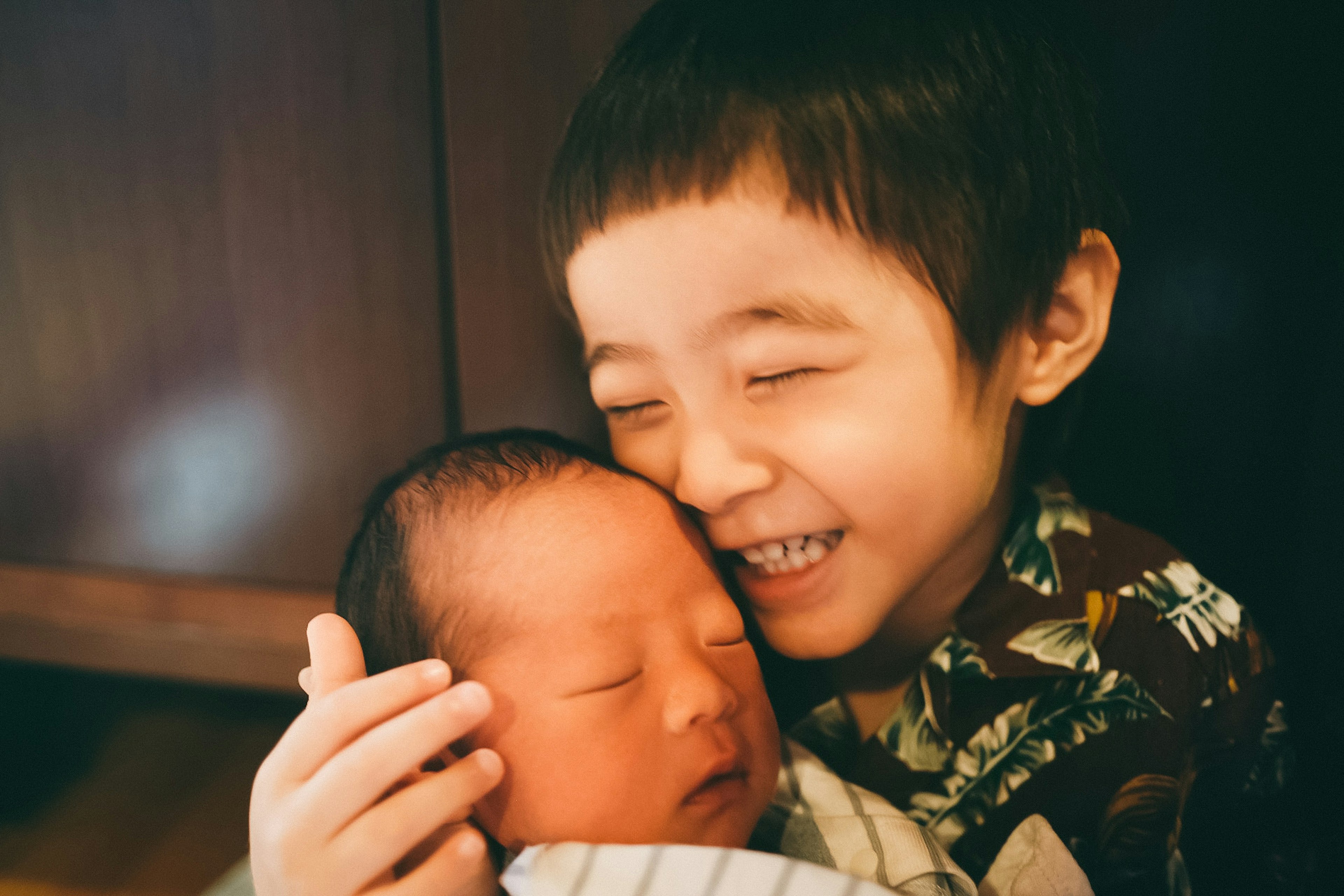 A joyful older brother hugging a sleeping baby