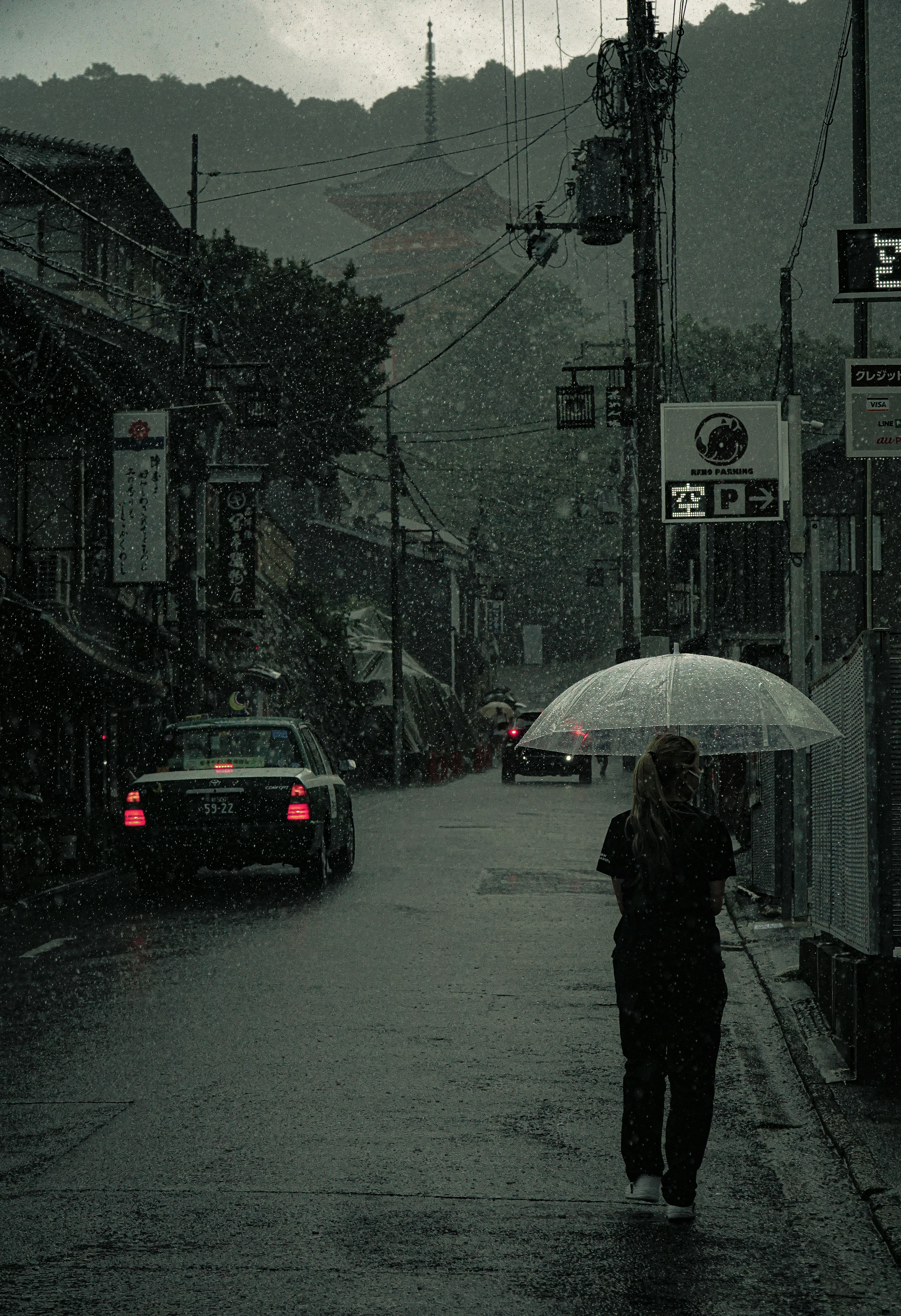 一位女性在雨中的街道上走，手持雨傘