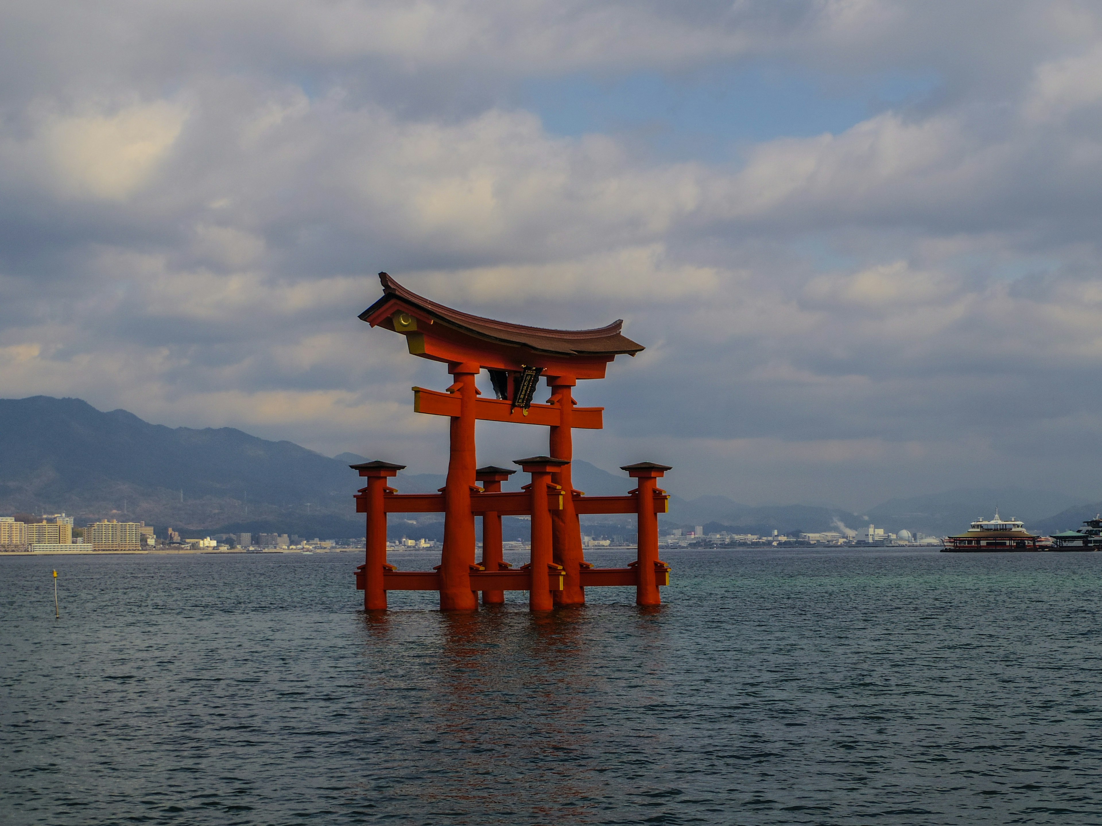 Gerbang torii merah mengapung di laut dengan latar belakang pegunungan