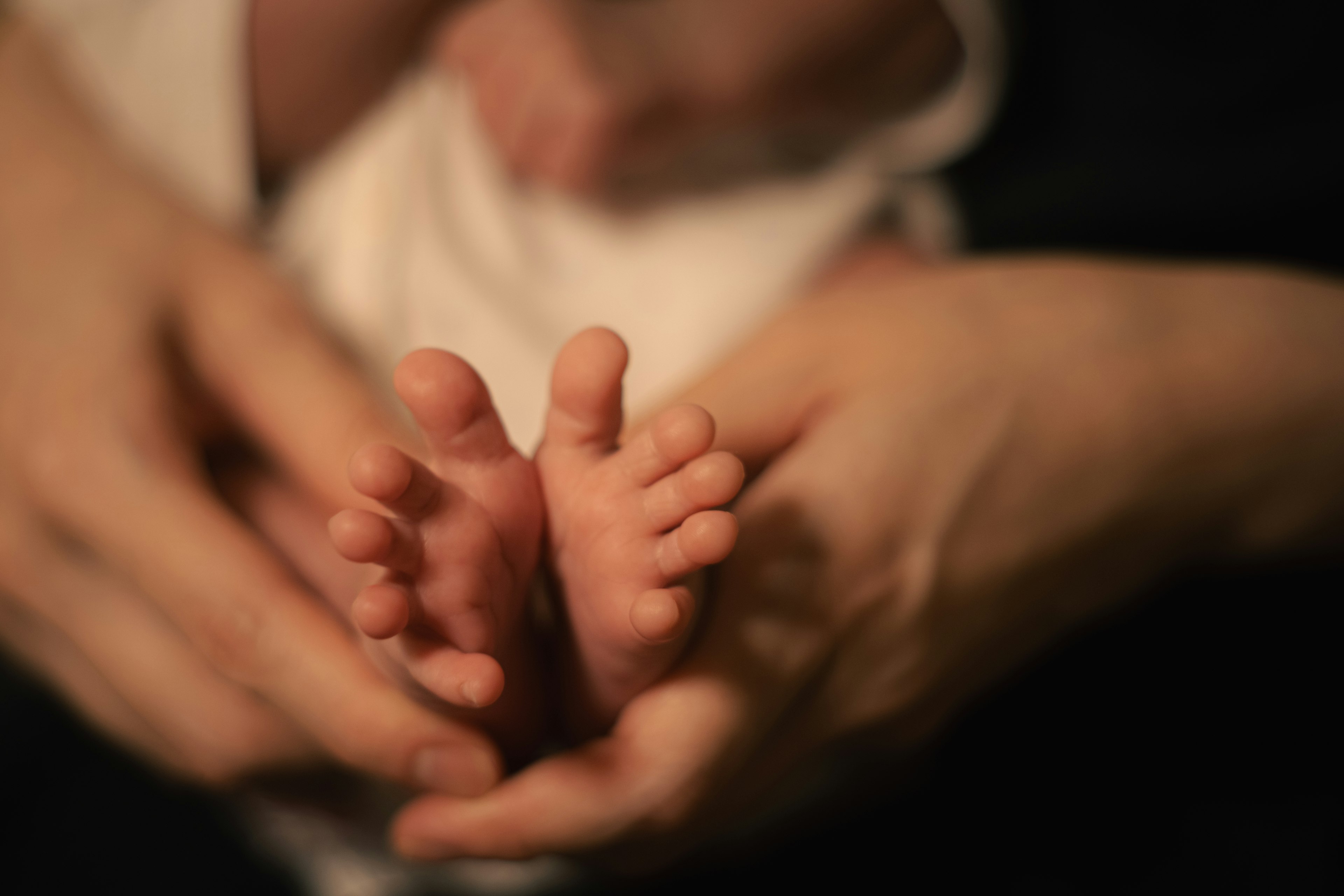 Gros plan des petits pieds d'un bébé tenus doucement dans des mains