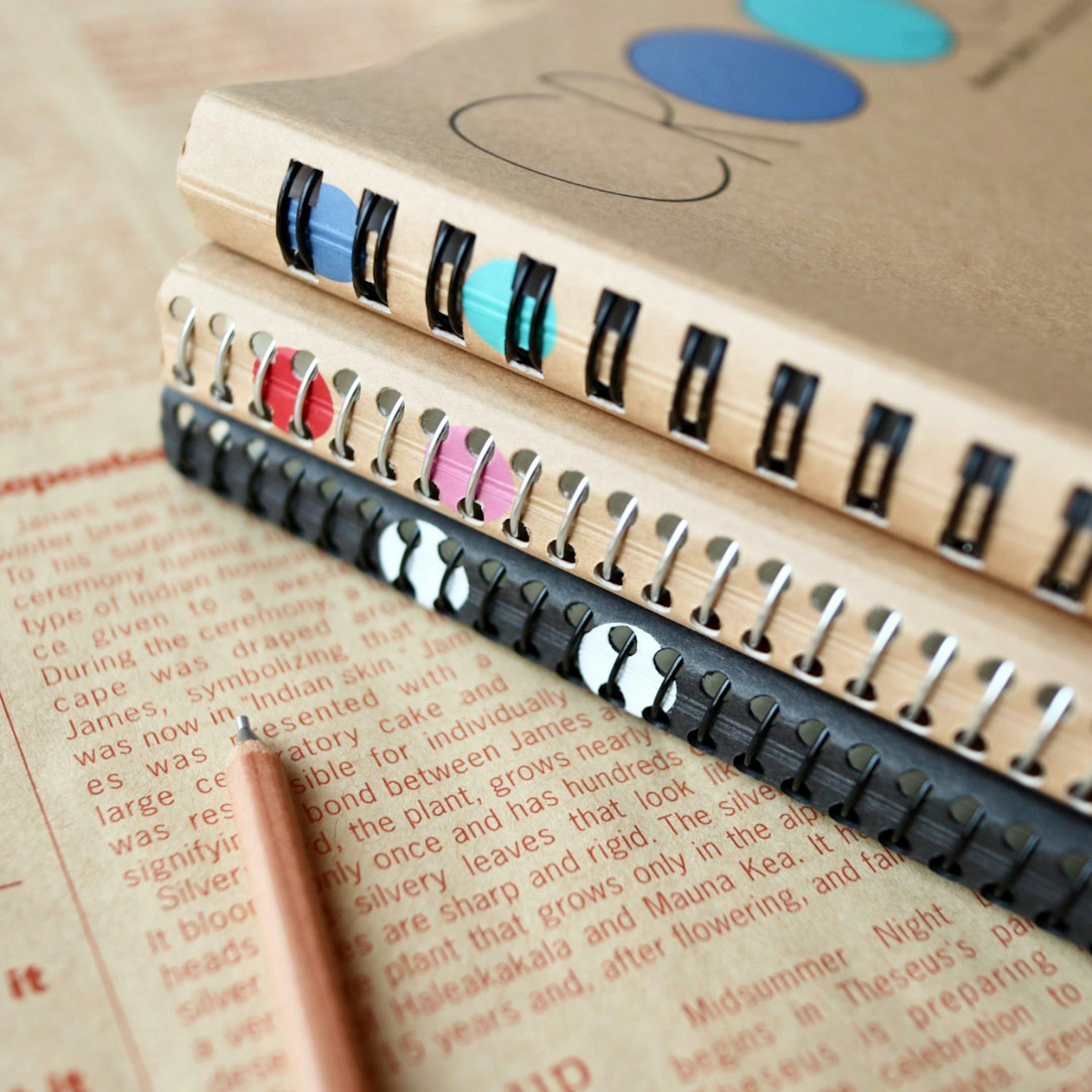 Stack of colorful notebooks with a pencil on lined paper featuring text