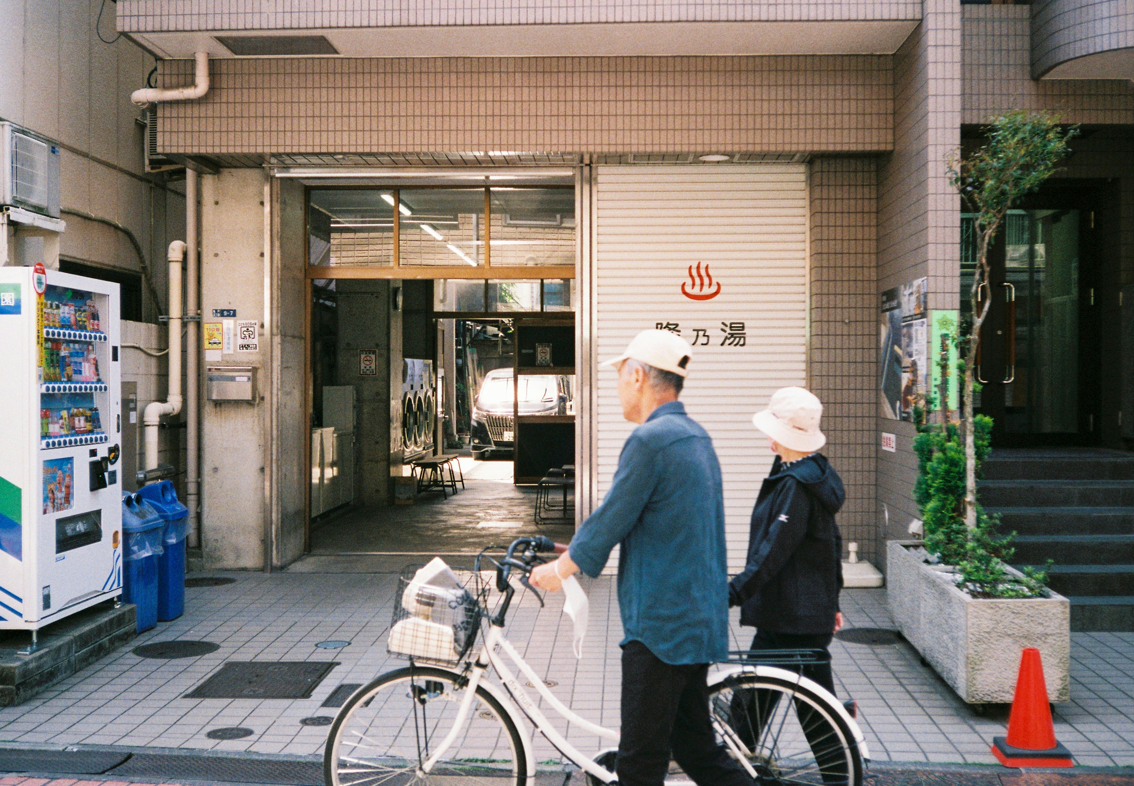 白い自転車を押す二人の高齢者が街を歩く