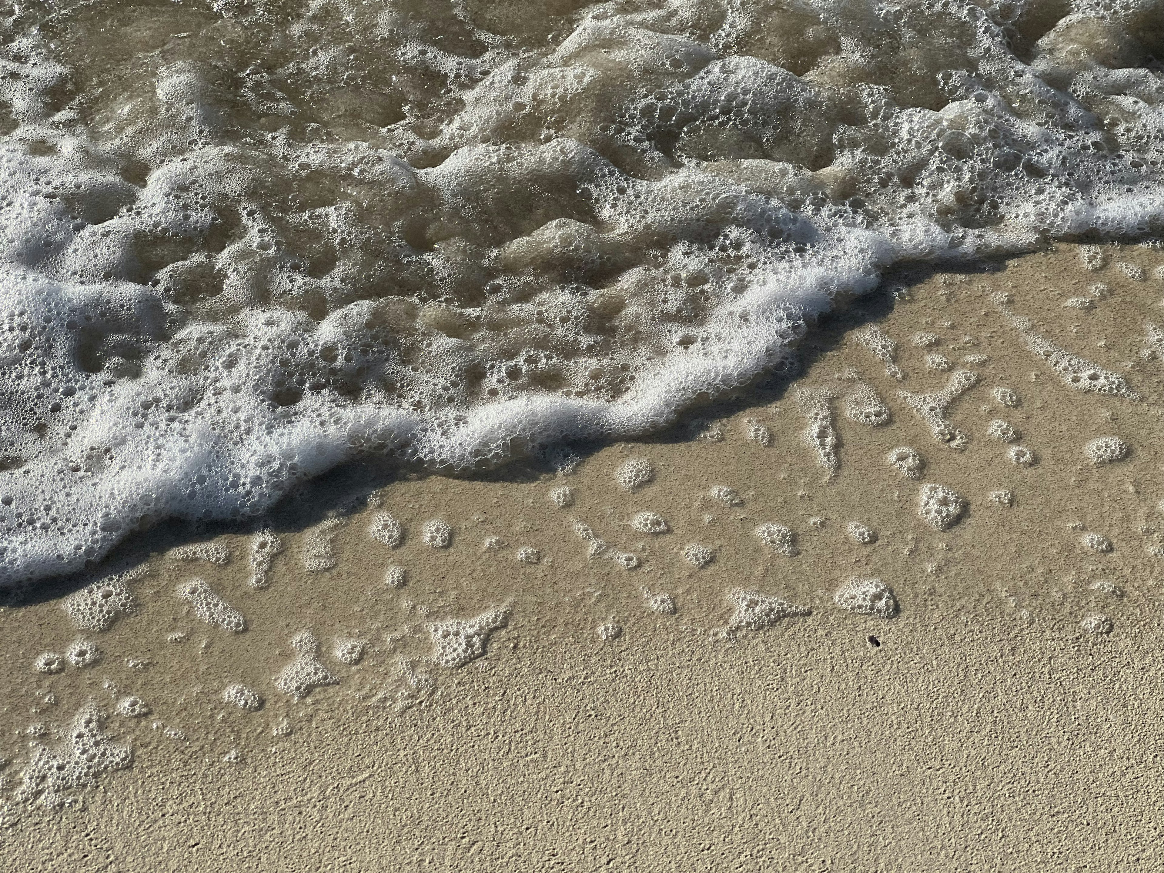 Close-up of beach sand with waves and foam