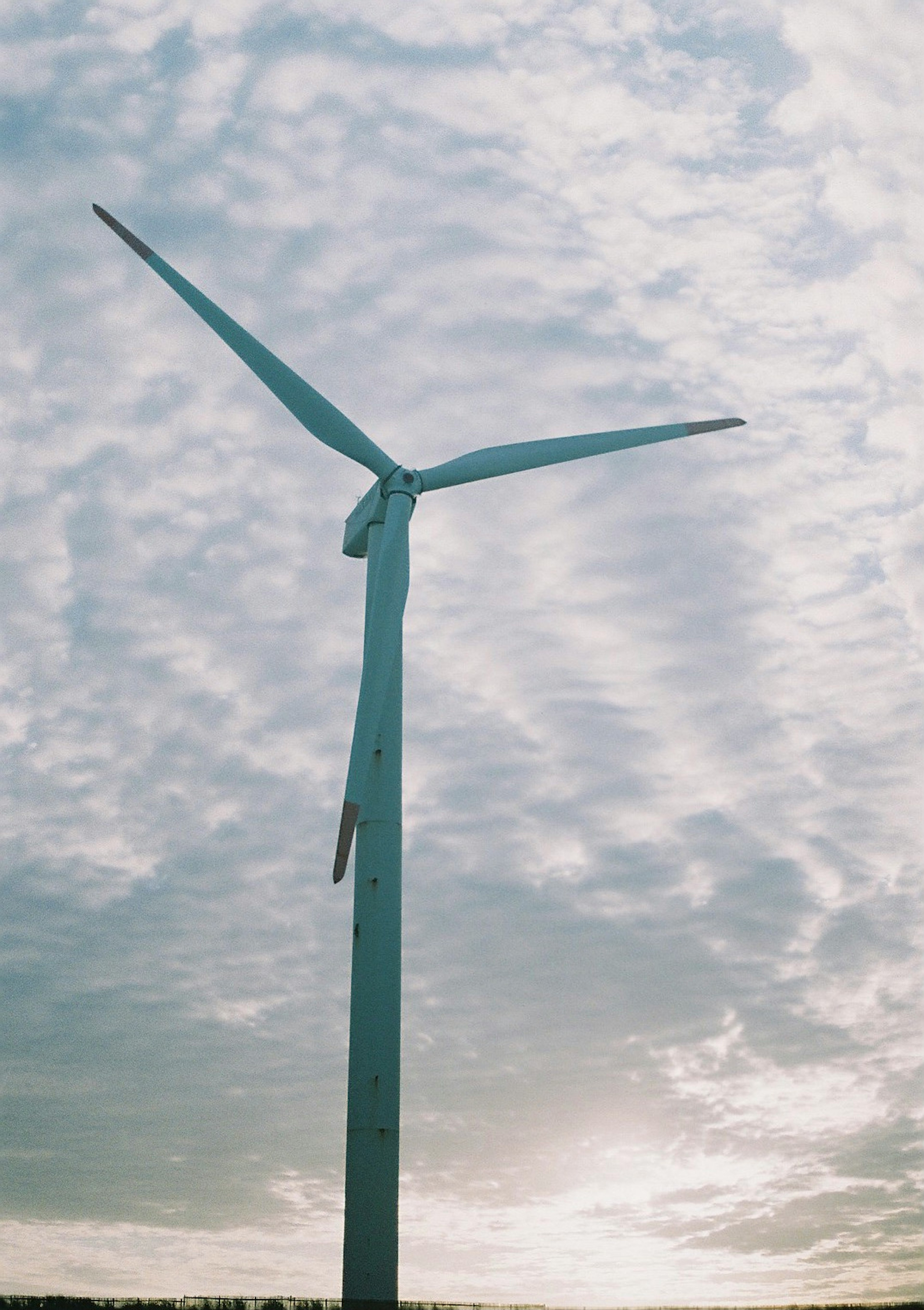 Una turbina eólica de pie bajo un cielo azul con nubes