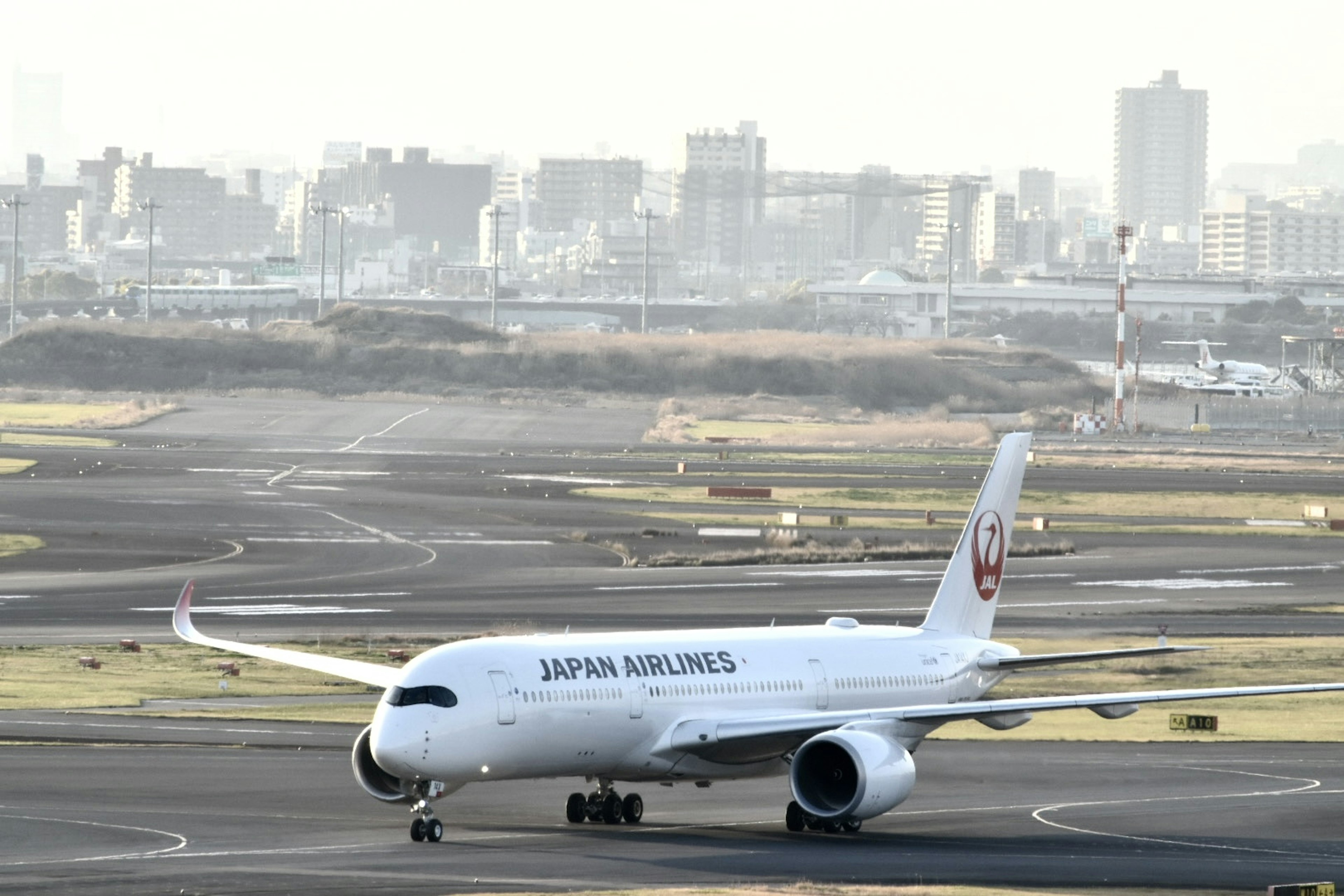 Máy bay Japan Airlines đang di chuyển trên đường băng với đường chân trời thành phố ở phía sau