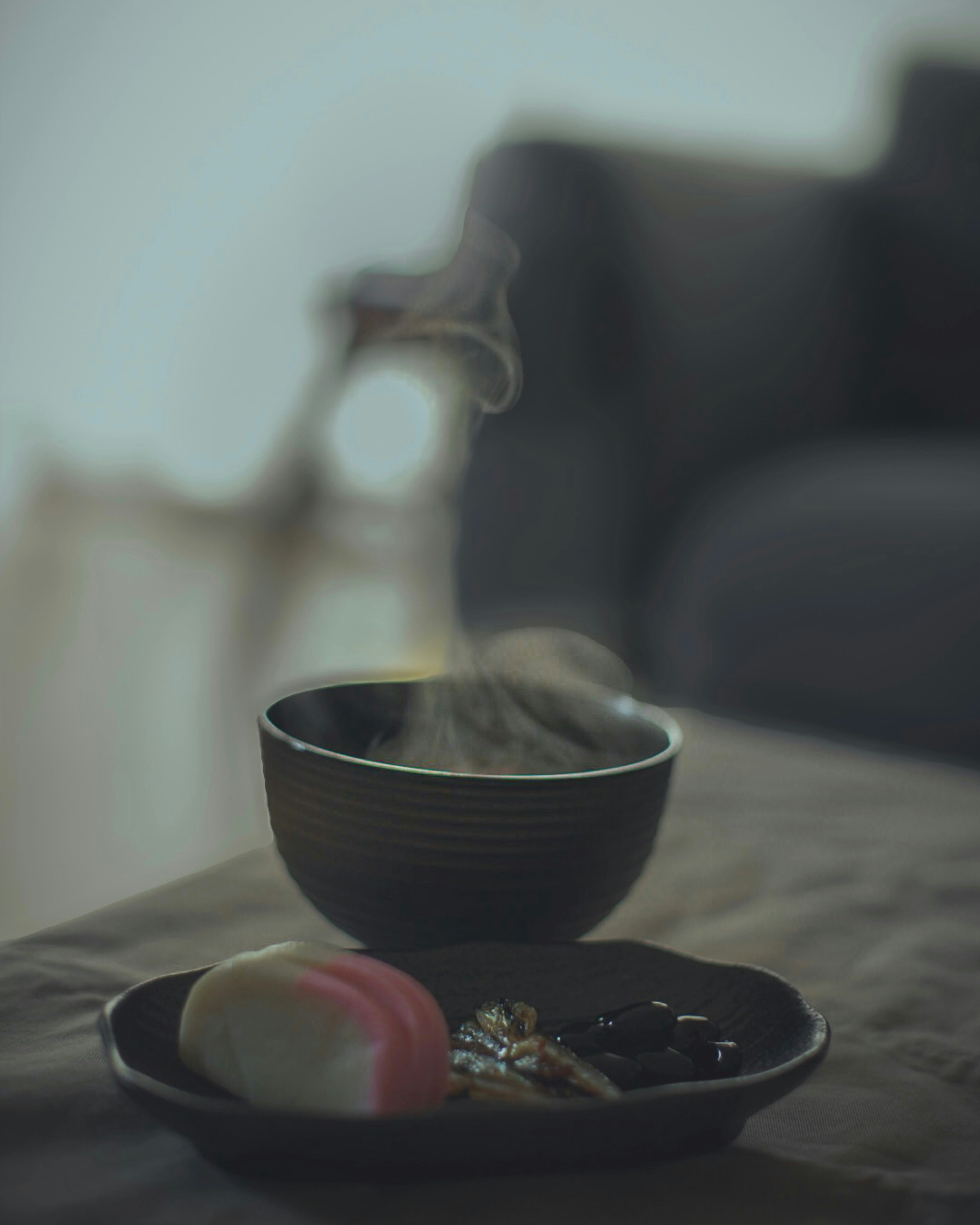 A serene table scene featuring a steaming black bowl and colorful Japanese sweets