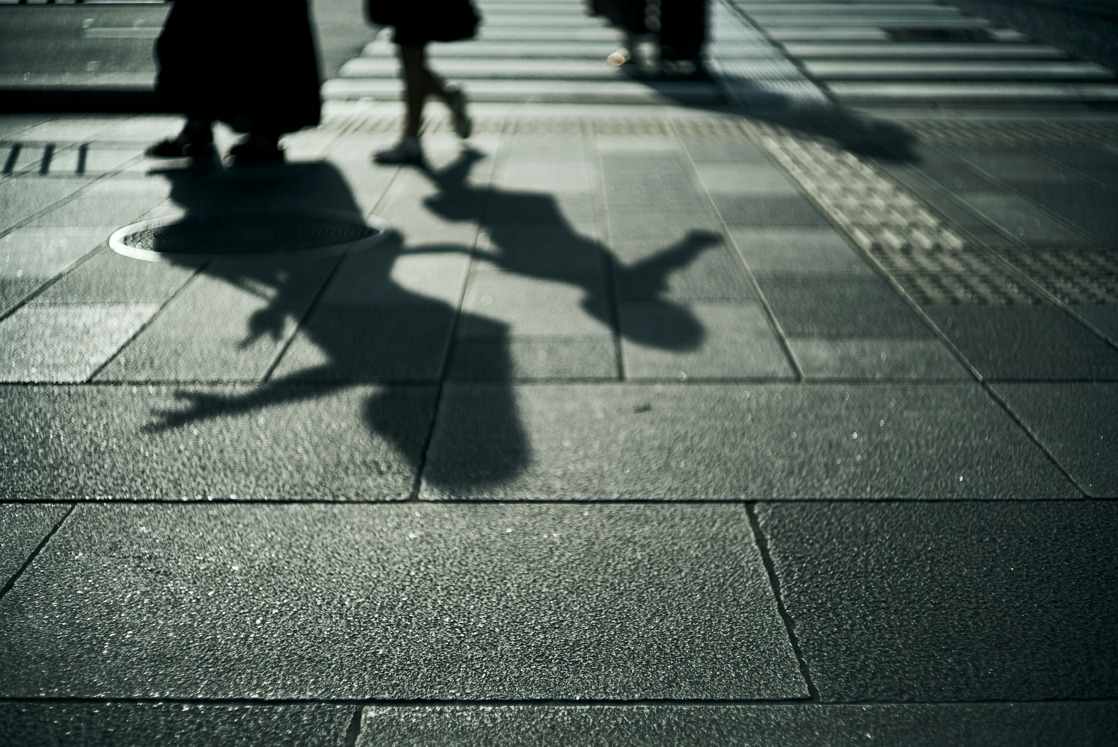 Shadows of pedestrians reflected on tiled pavement at a crosswalk