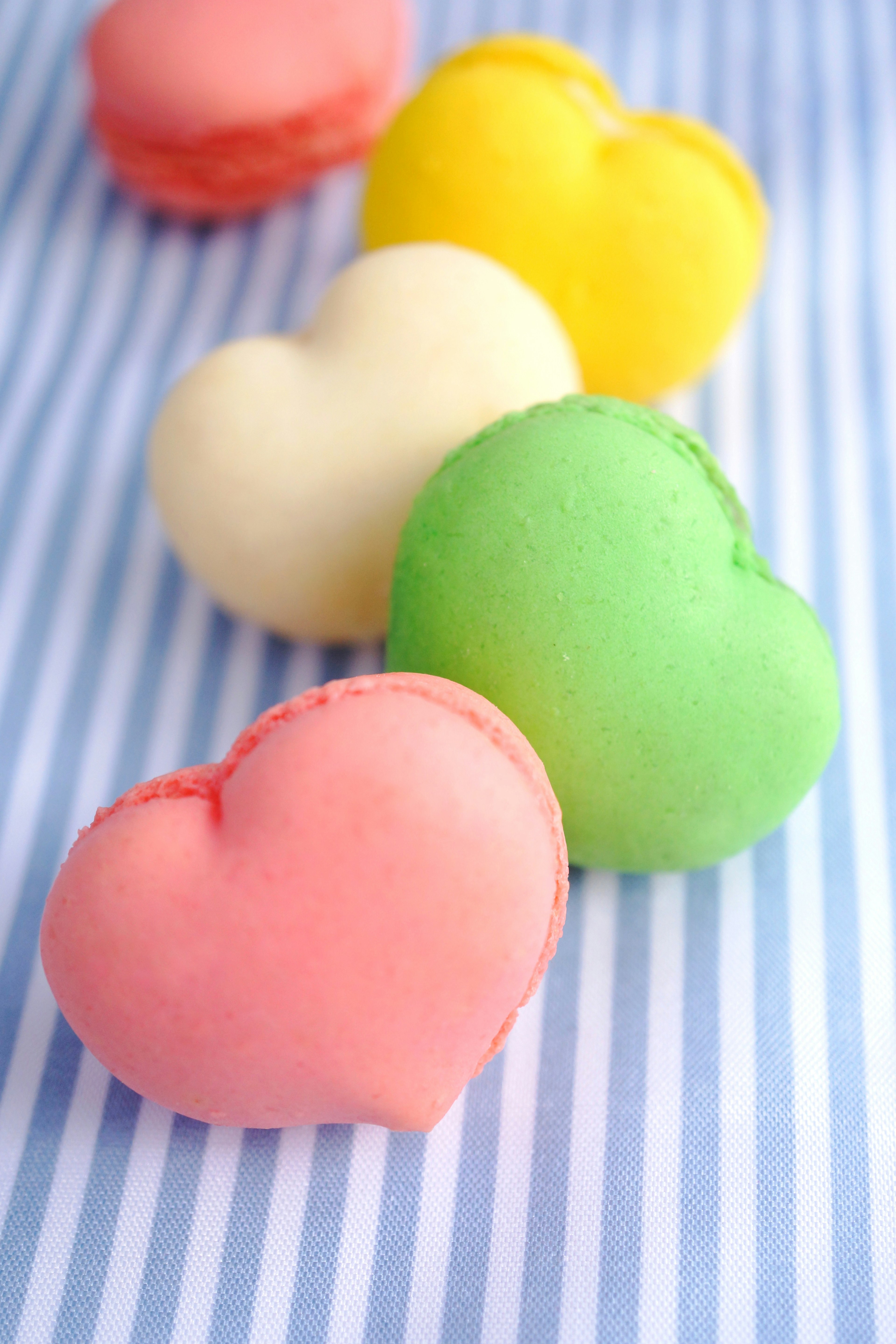 Colorful heart-shaped macarons arranged on a blue and white striped background