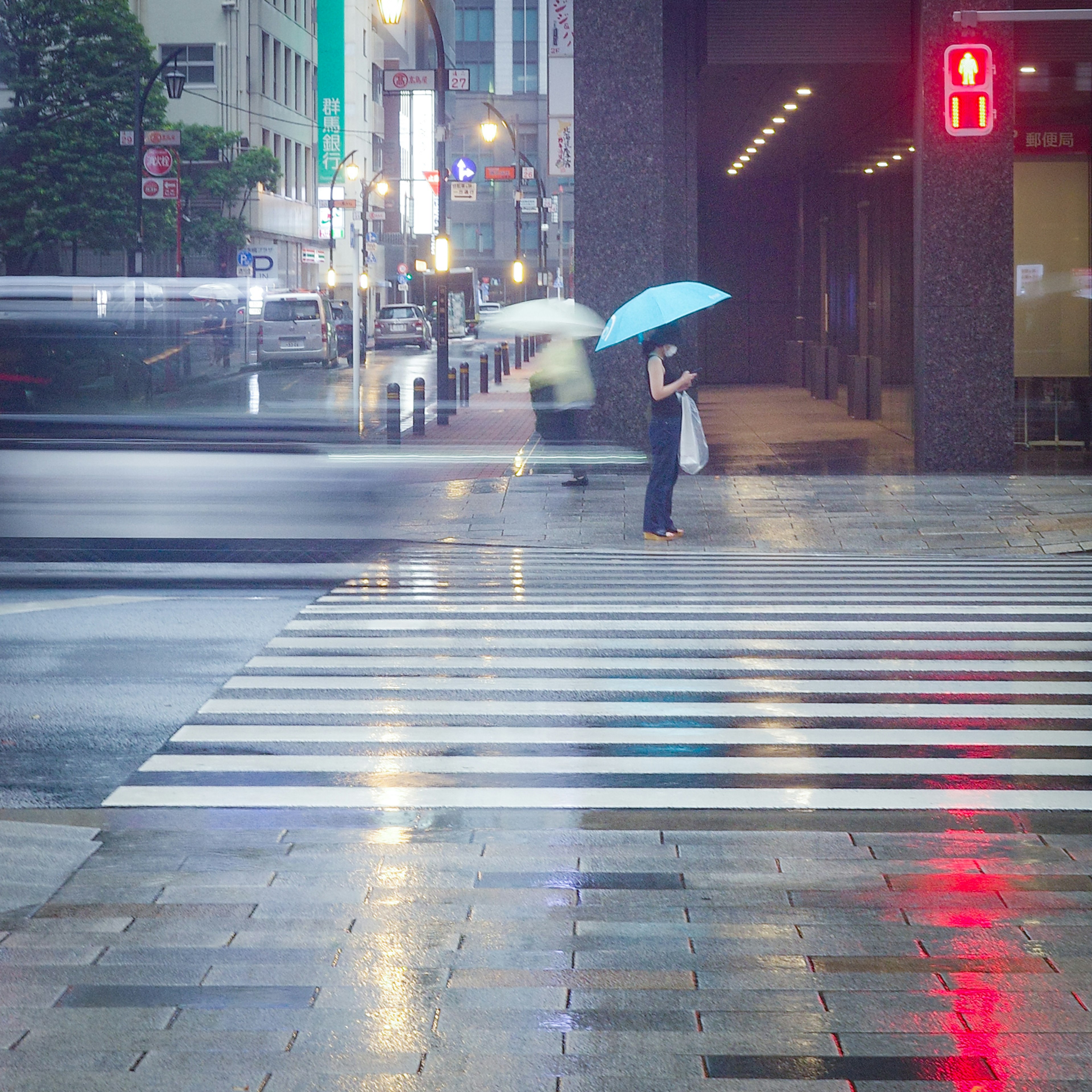 雨の中で傘を持つ人が横断歩道に立っているシーン