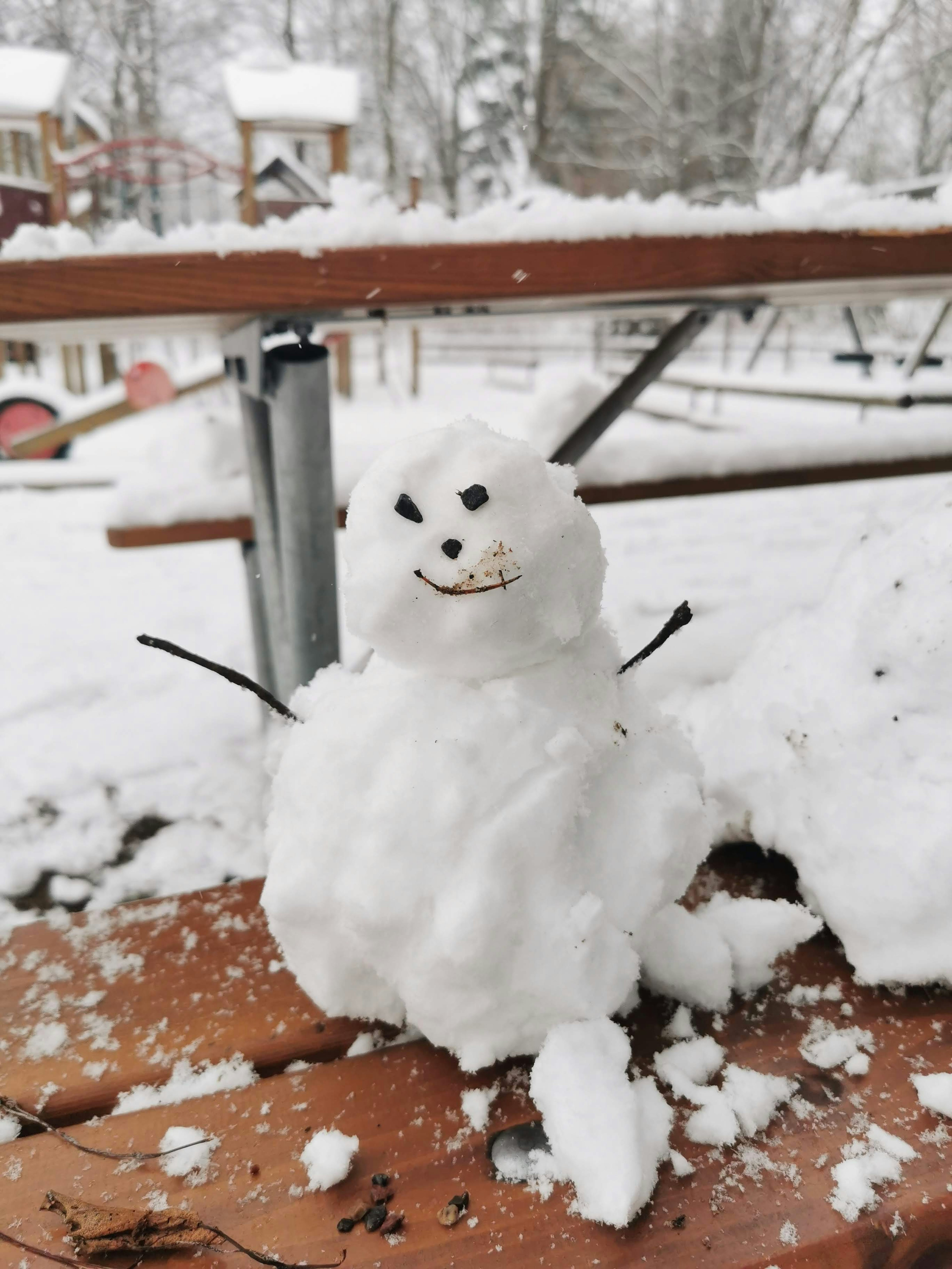 Ein kleiner Schneemann aus Schnee steht auf einem Holztisch