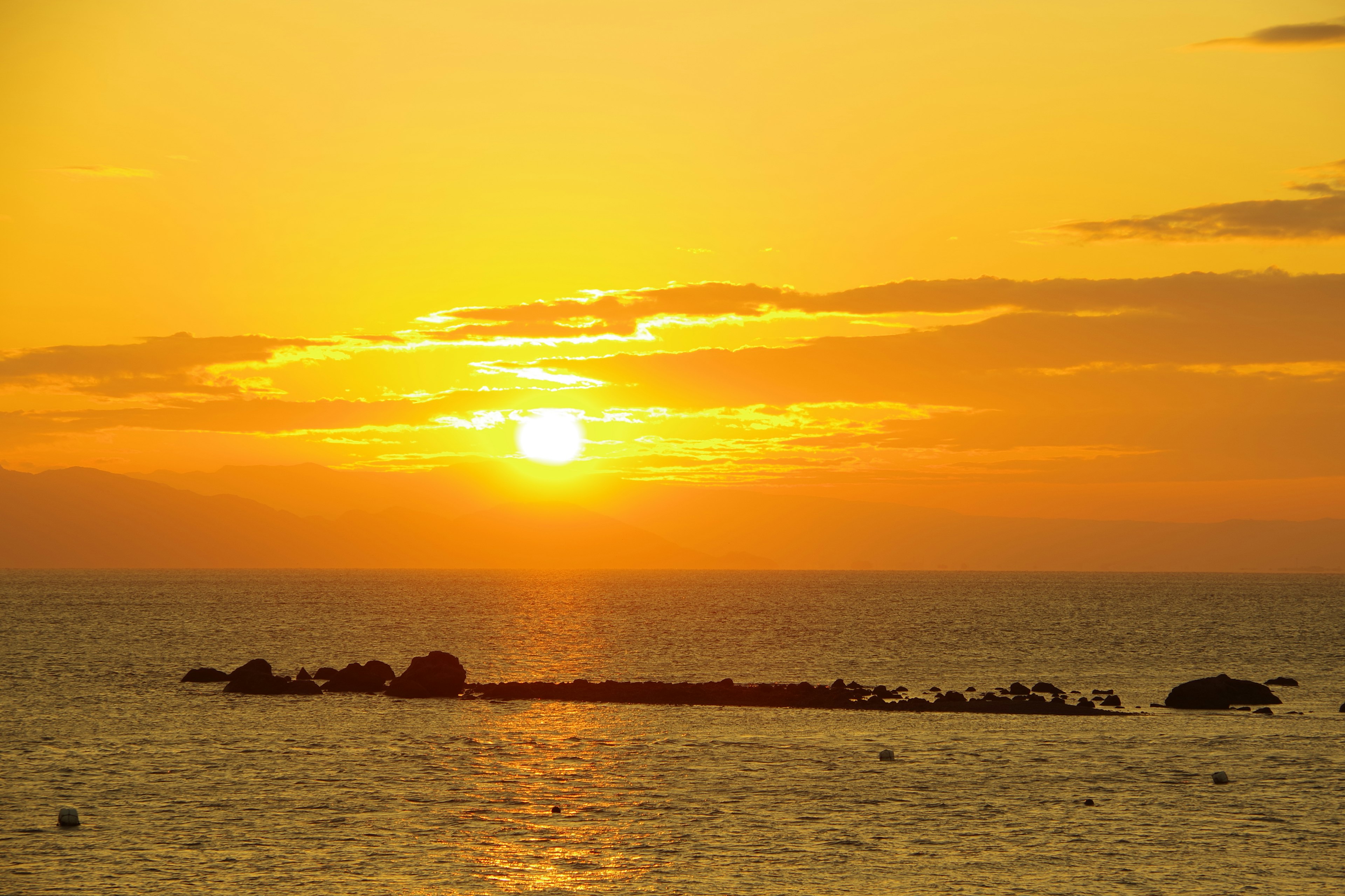 Atardecer sobre el océano con nubes naranjas y rocas distantes