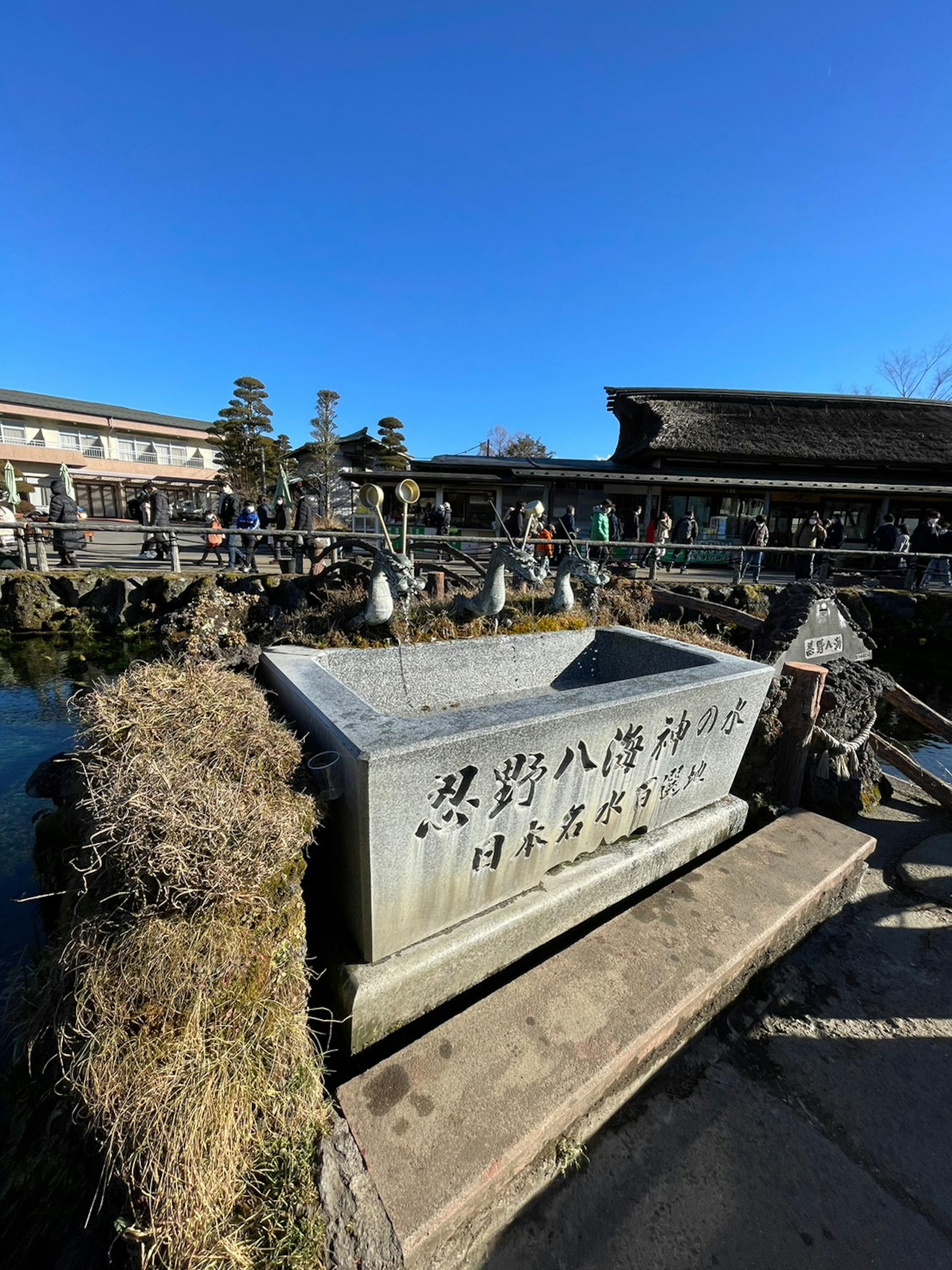 古い石の水槽と青い空の下で人々が集まる風景