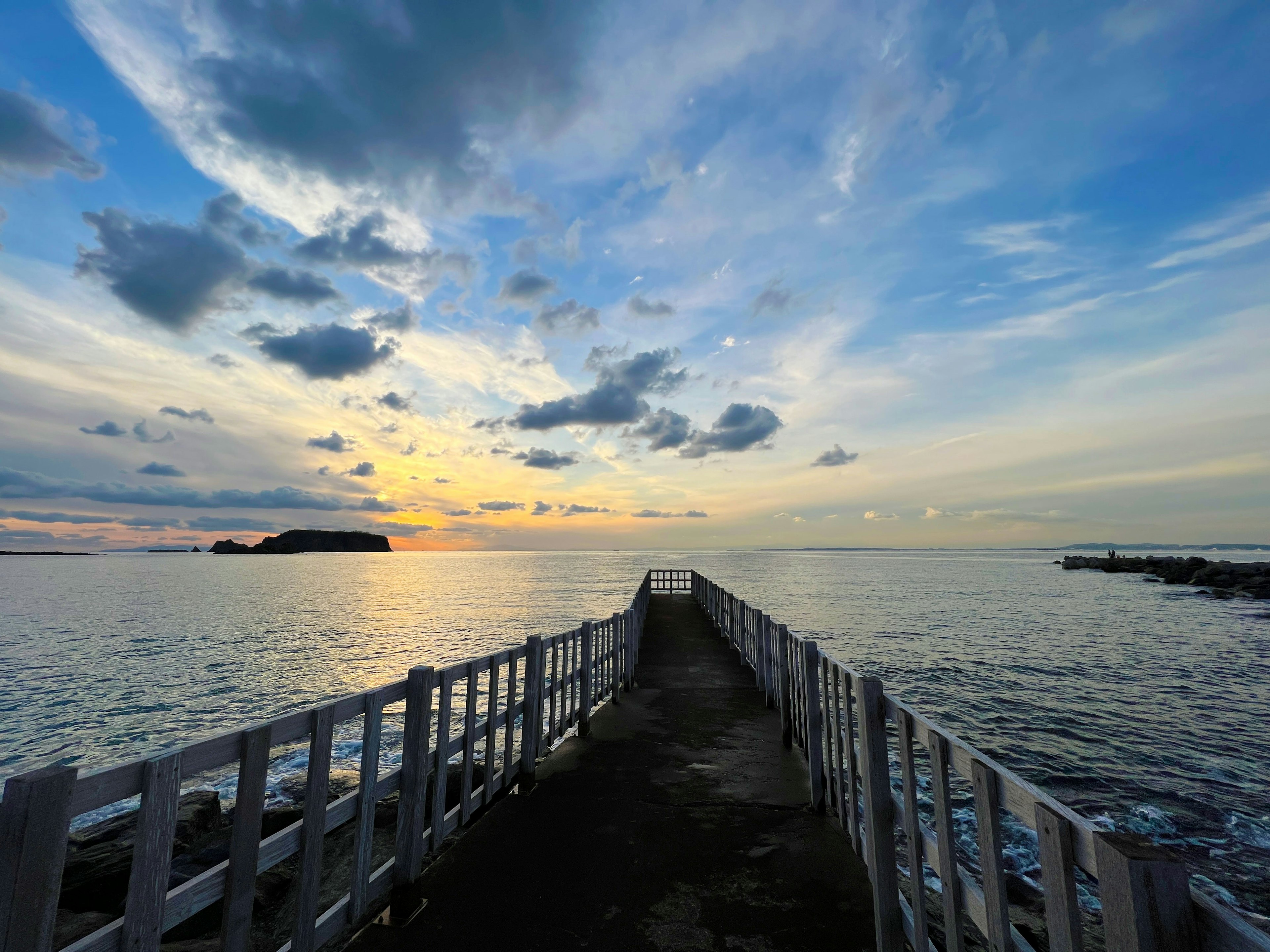 Dermaga putih yang mengarah ke laut dengan langit matahari terbenam yang indah