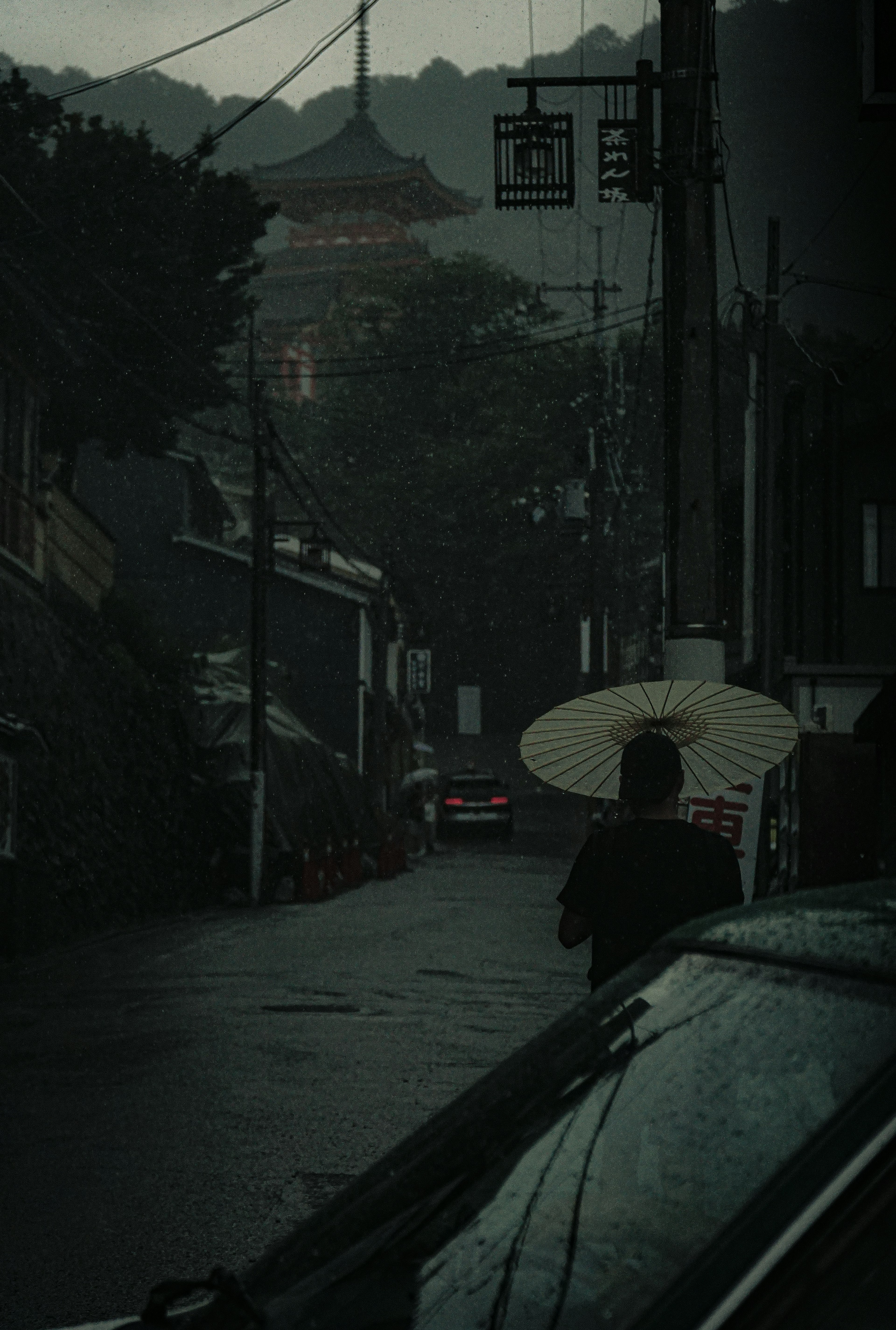 A person walking with an umbrella on a dark street with buildings in the background