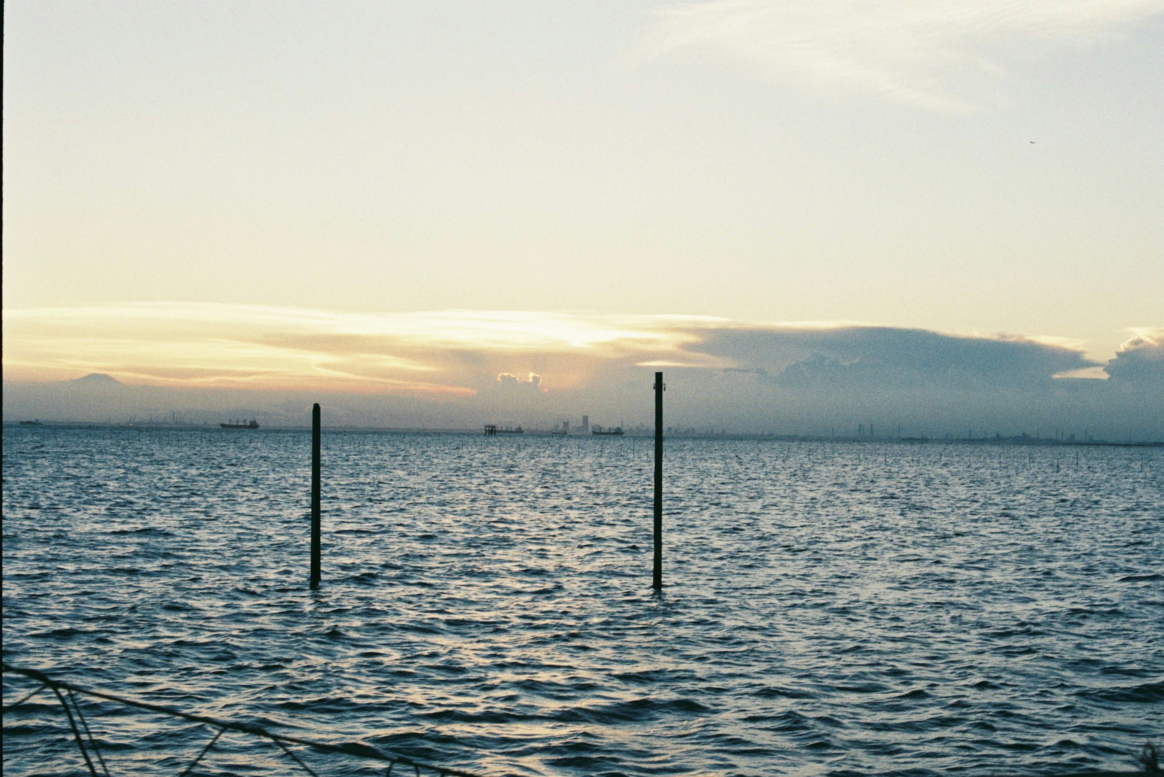 Vista panoramica del mare e del cielo con pali nell'acqua calma e luce soffusa del tramonto