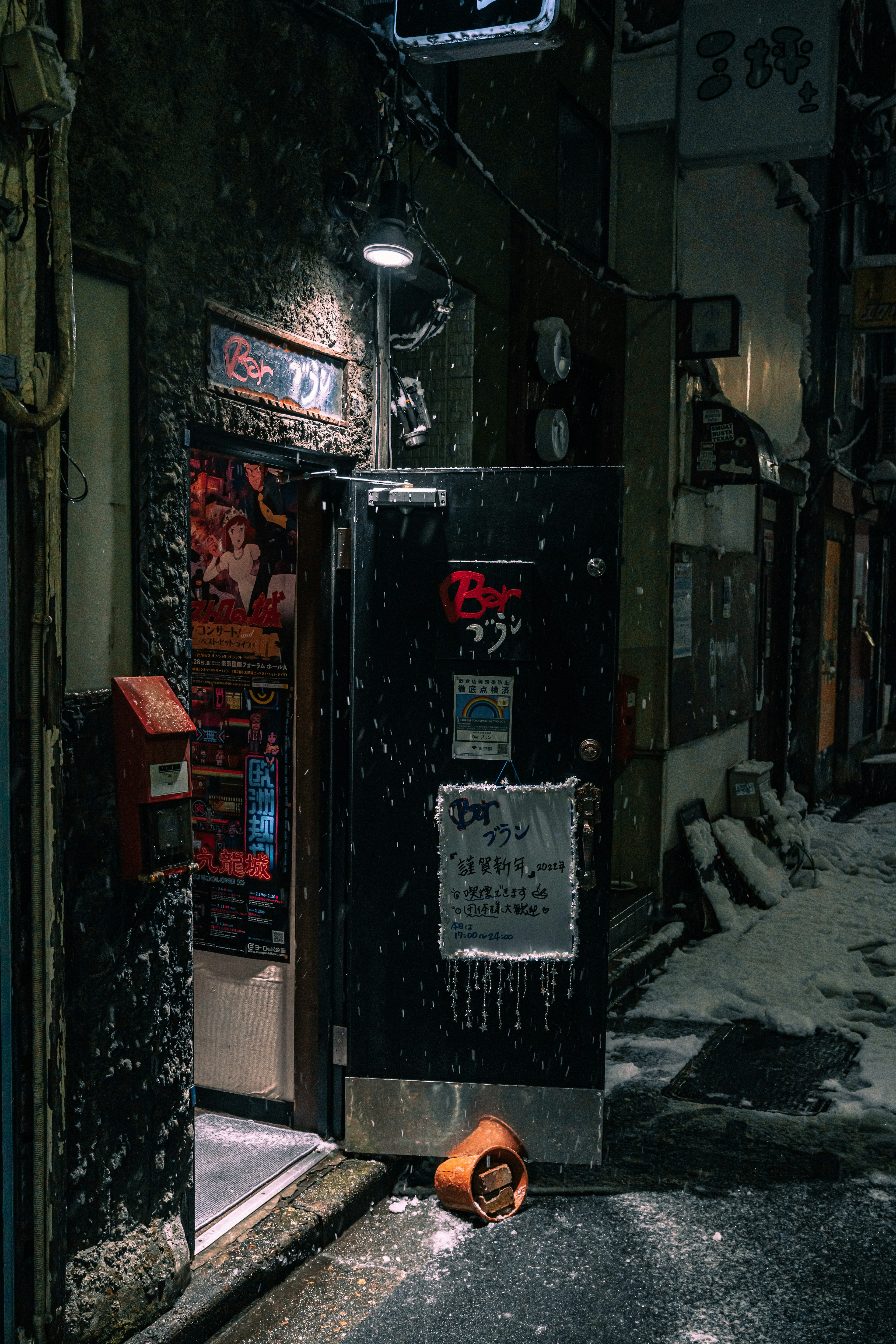 Entrance of a small shop on a snowy night with a red mailbox