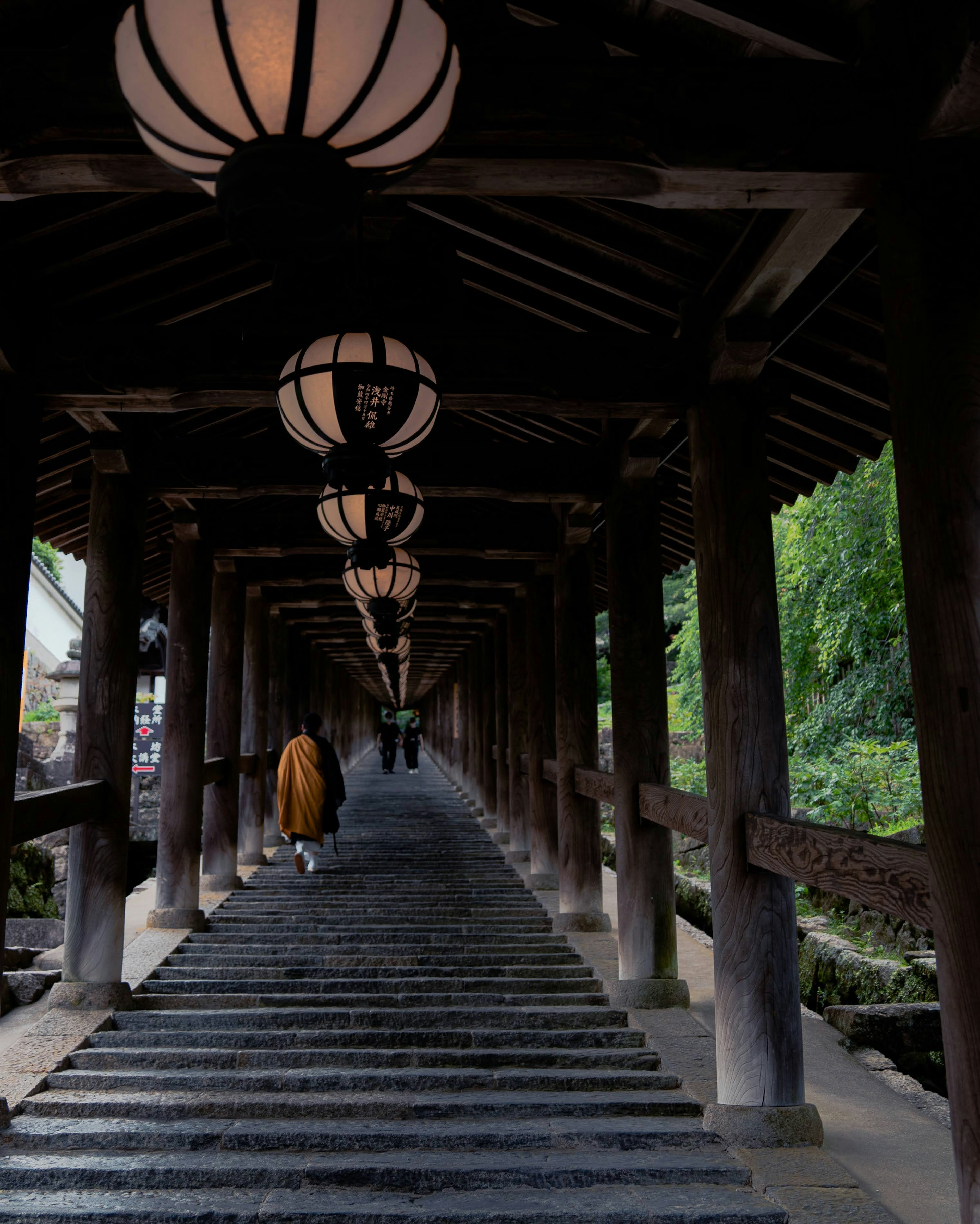 A person walking on stone steps beneath lanterns in a wooden arcade