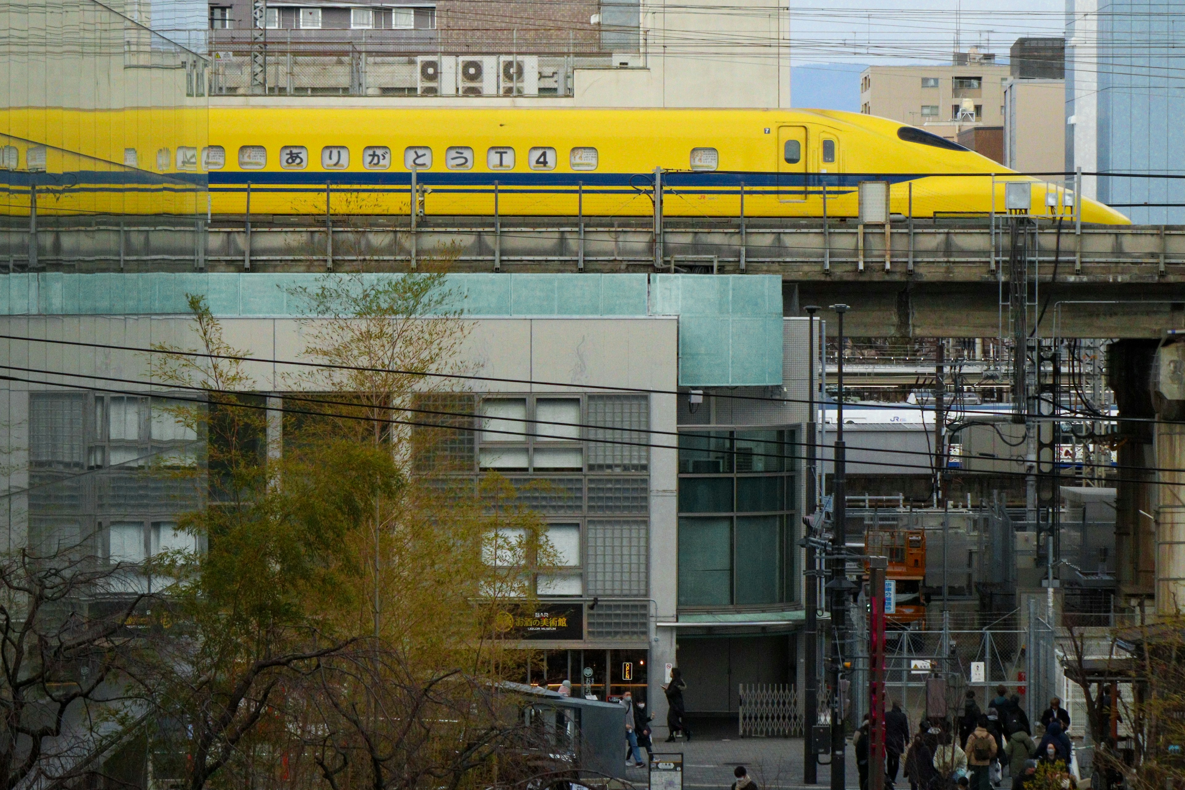 A yellow Shinkansen train traveling between urban buildings