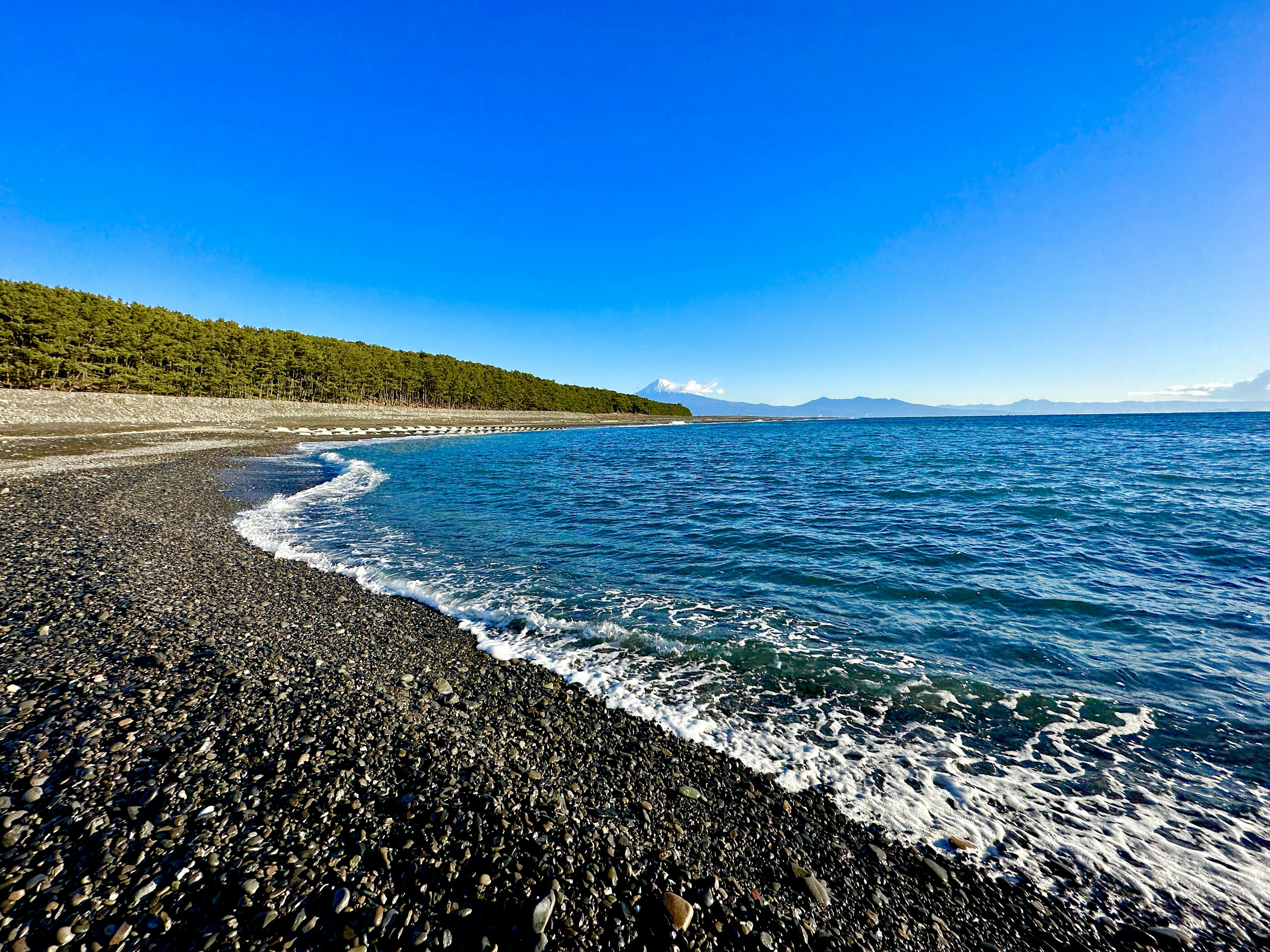 Landschaftsansicht eines Kiesstrandes unter einem hellblauen Himmel mit ruhigen Ozeanwellen