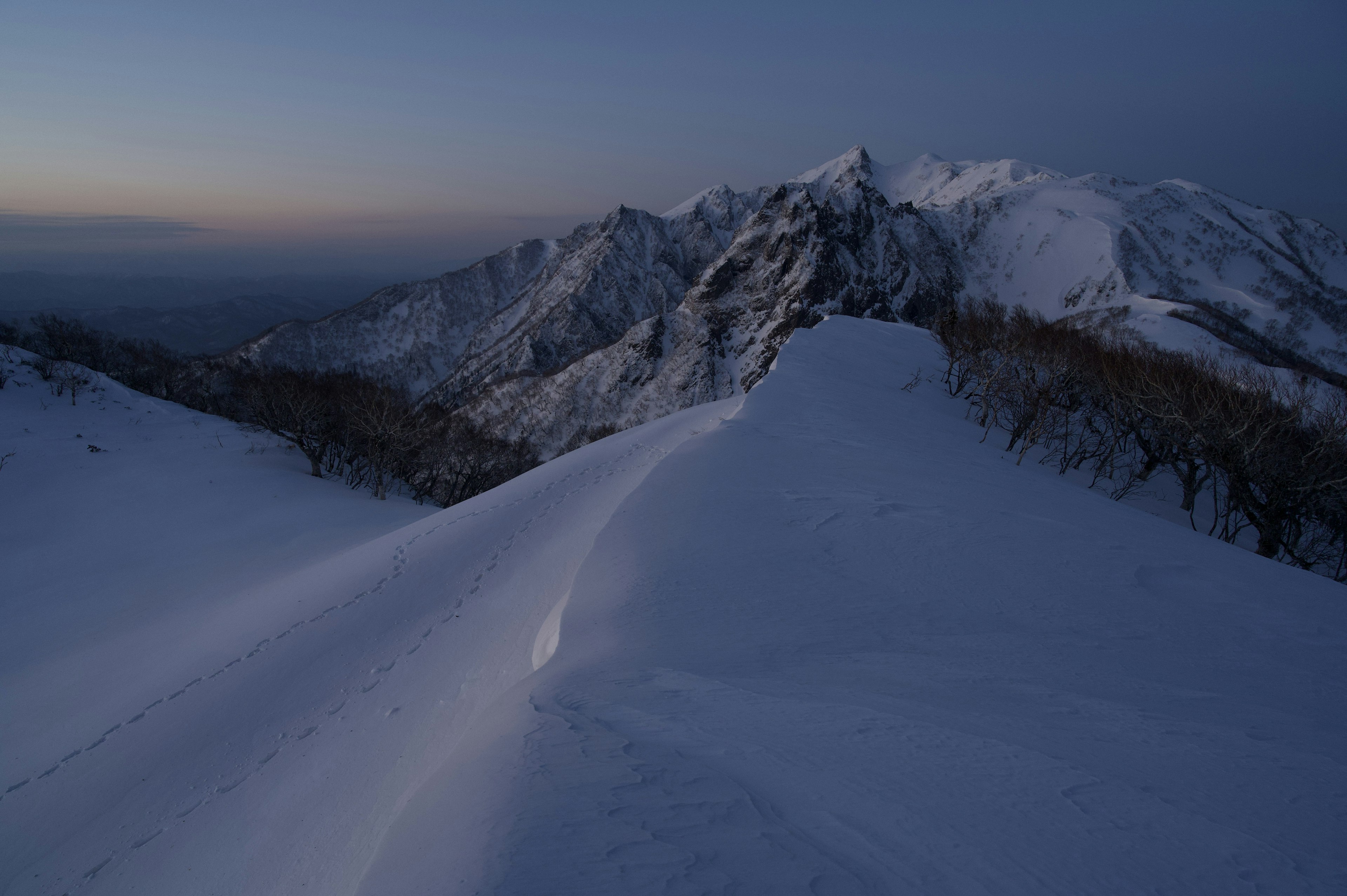 Snowy mountain landscape under twilight with rugged peaks